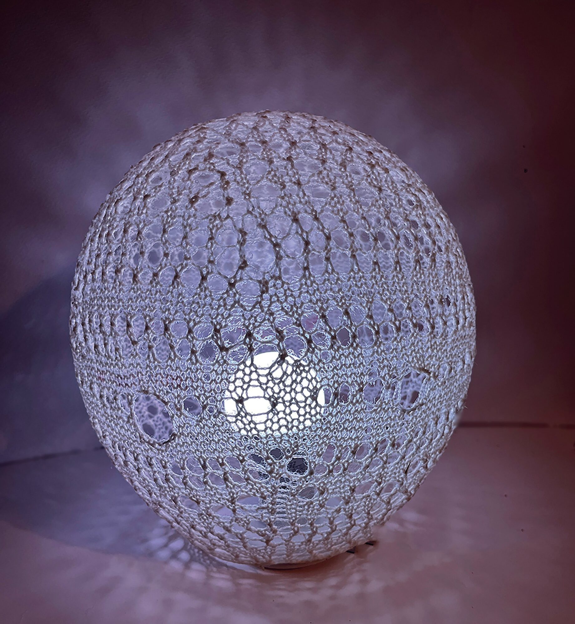 Spherical object with a textured, lattice-like surface, illuminated from within, casting light and shadows around it.
