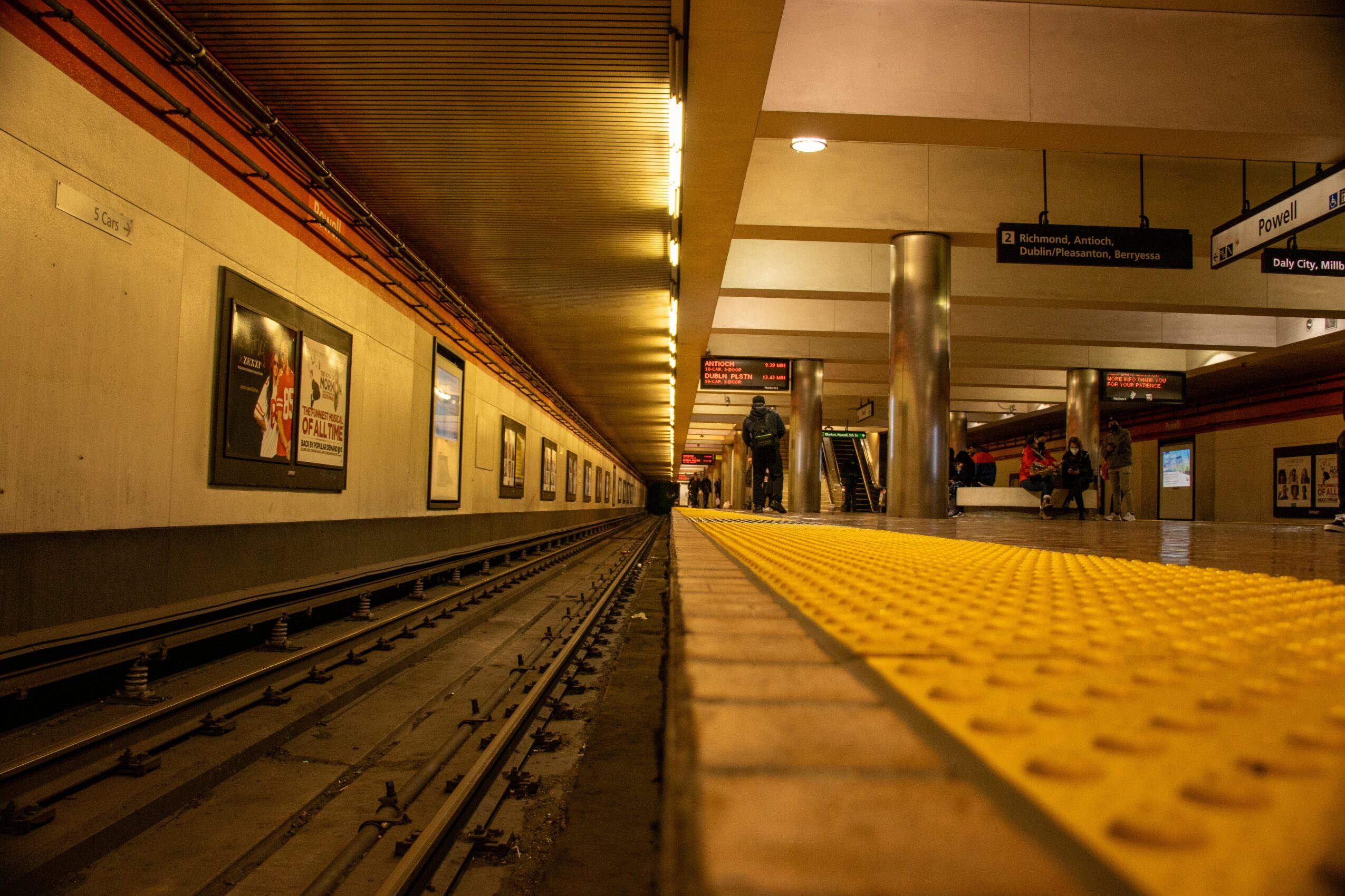 Underground subway station with tracks, platform, and people waiting, viewed from a low angle.
