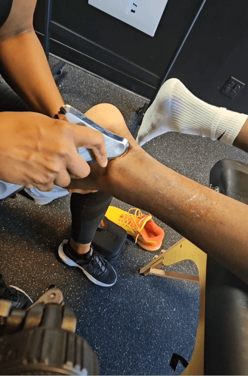 Person applying a bandage or medical treatment to a person's leg, which is elevated and supported by a chair.
