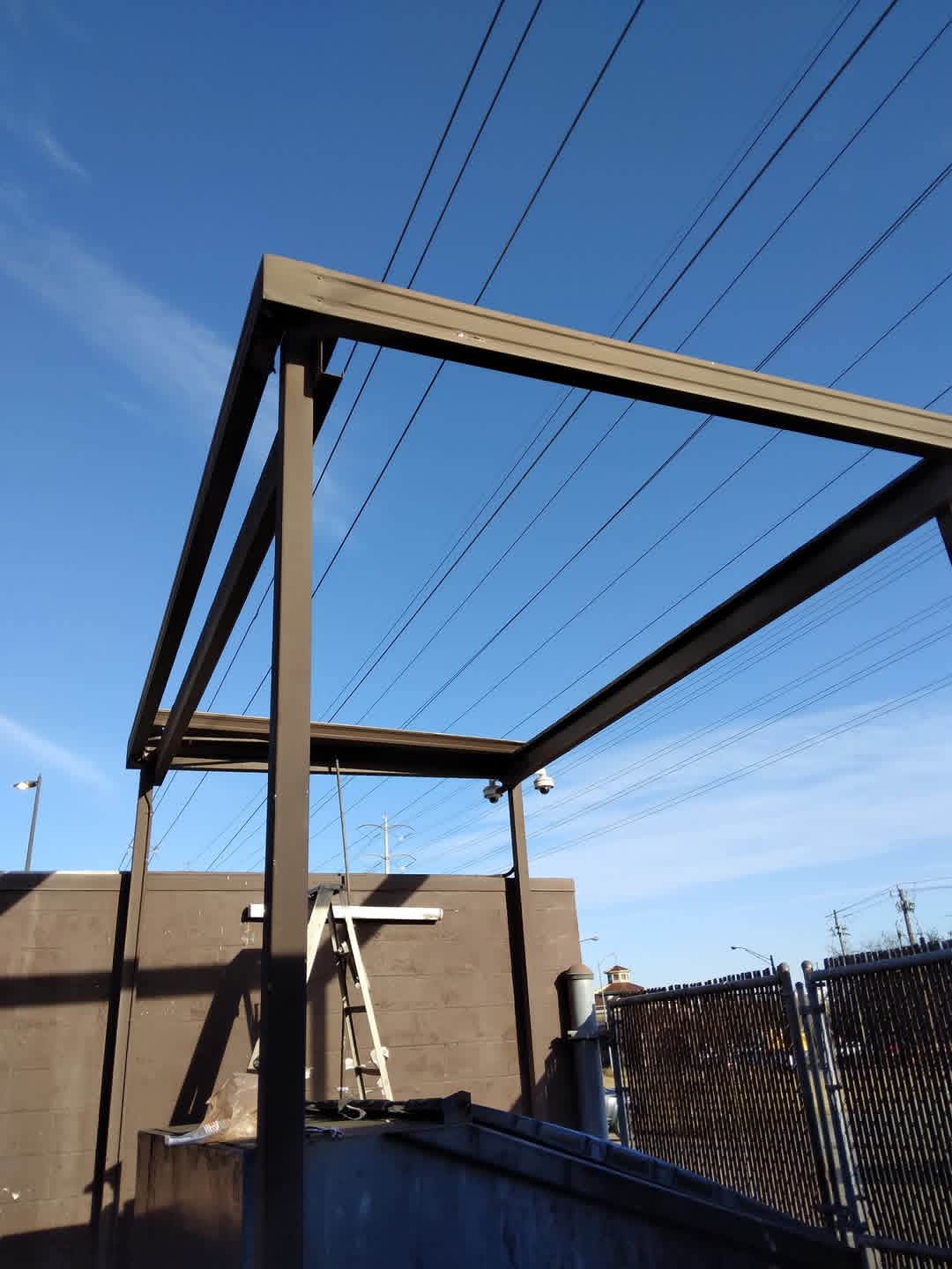 Metal frame structure outdoors with power lines and a building in the background under a blue sky.