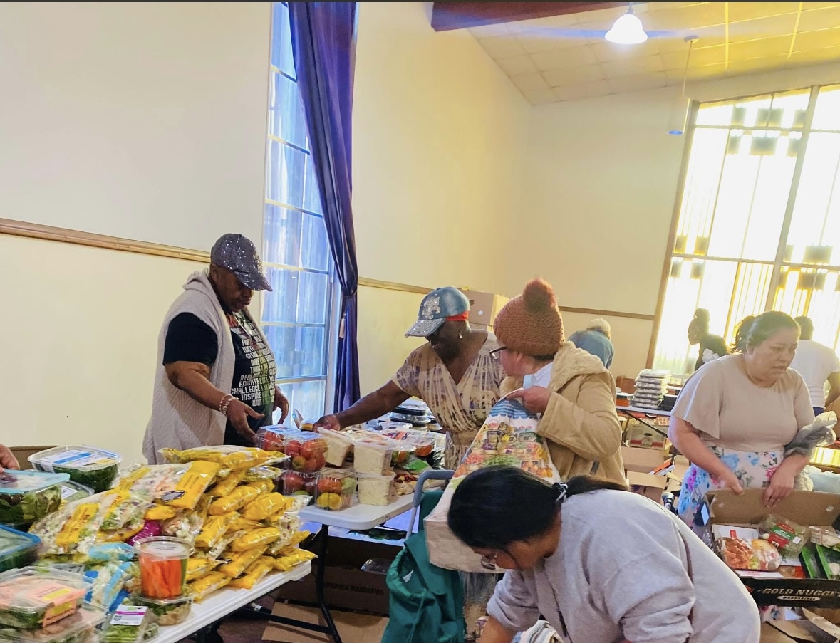 People shopping at a market stall with snacks and goods, inside a room with large windows and natural light.