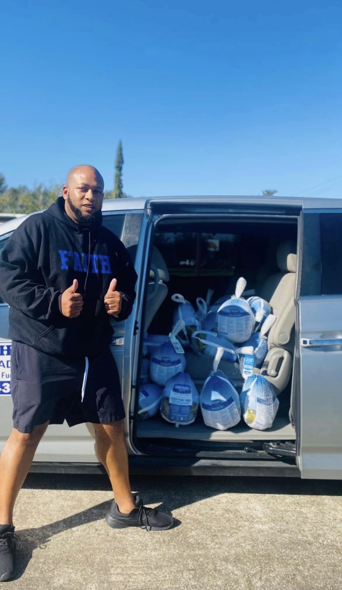 Man standing next to a vehicle with open sliding door filled with bags and supplies, outdoors on a sunny day.
