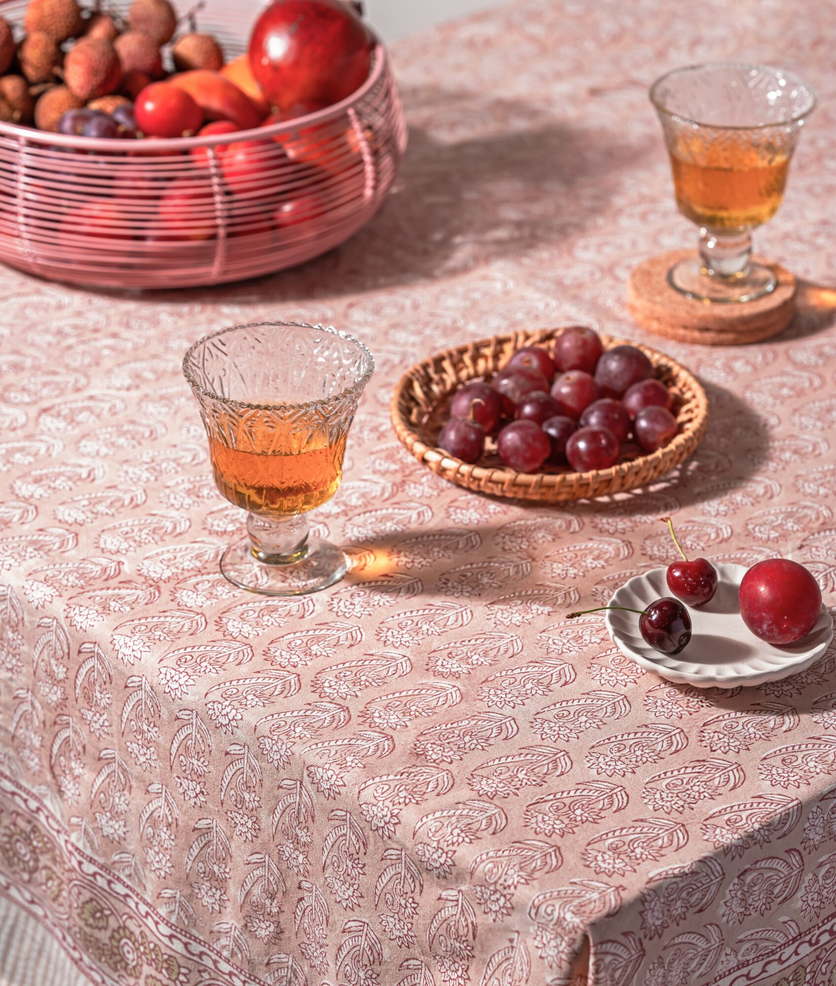 Table with grapes, glasses of drink, and a bowl of mixed nuts on a patterned tablecloth.
