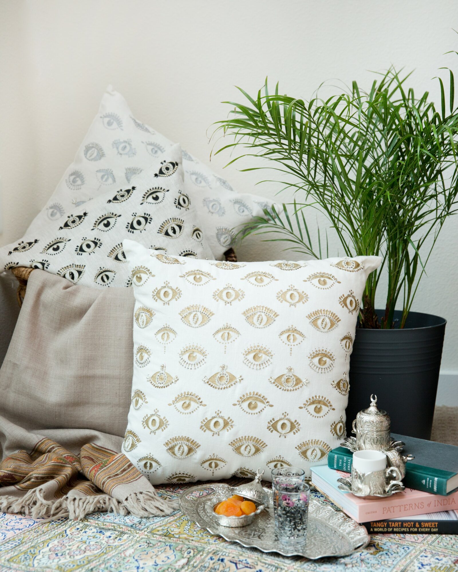 Pillow with eye pattern, potted plant, books, and decorative items on a bed or surface.