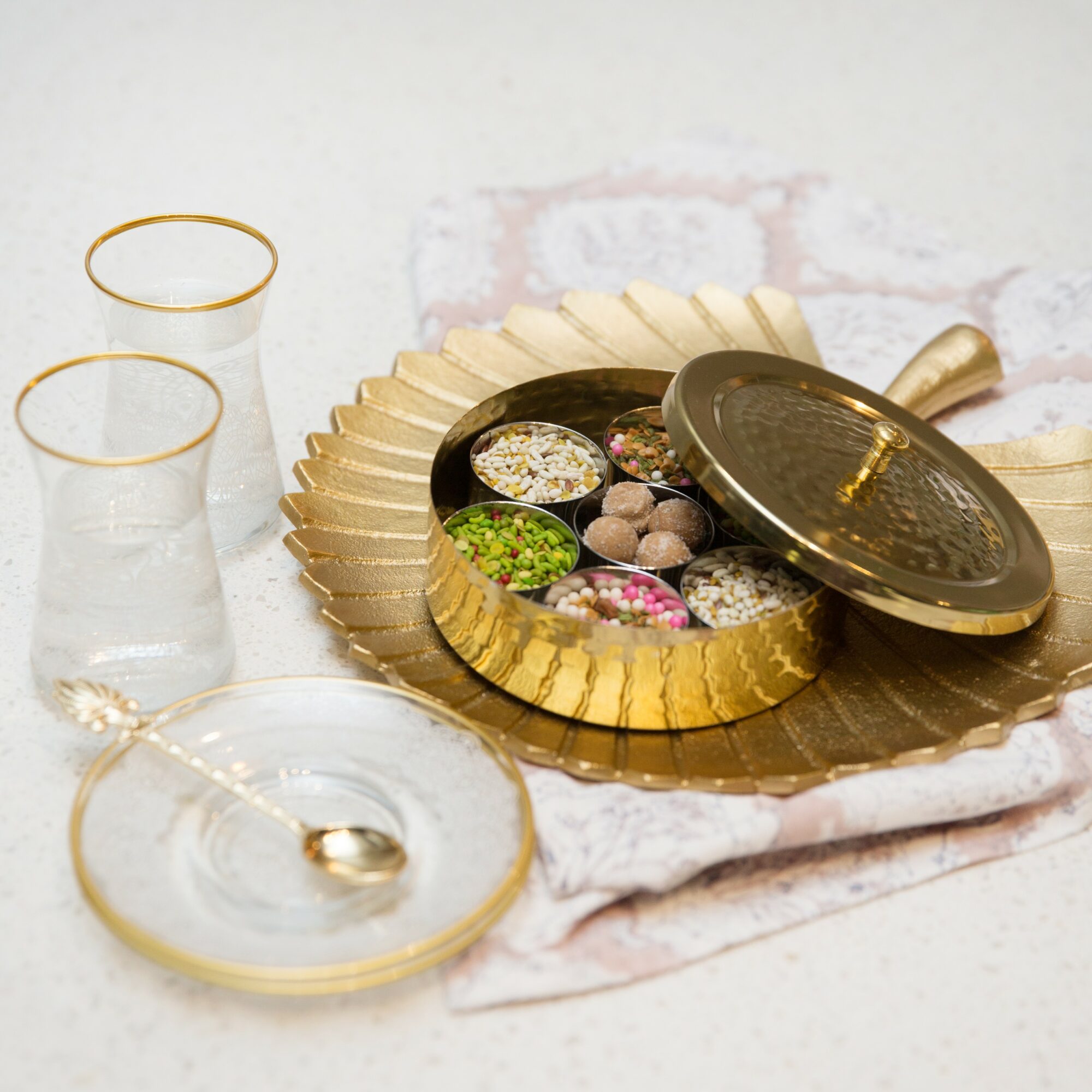Gold and black jewelry box with jewelry inside, two glasses of water, and a small dish with a spoon on a table.