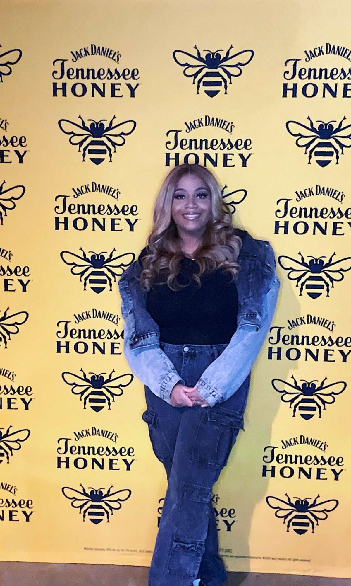 Woman with long hair smiling, standing in front of a yellow background with black bee and text pattern.