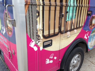 Close-up of a colorful vehicle with a black metal fence and clothing hanging inside, pink and blue design elements, and white footprints.