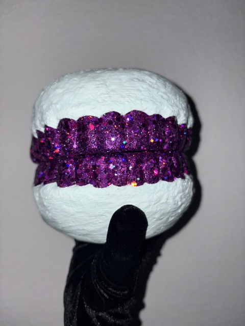 Person wearing a black glove holds a white textured object with a purple glittery strip in the center.