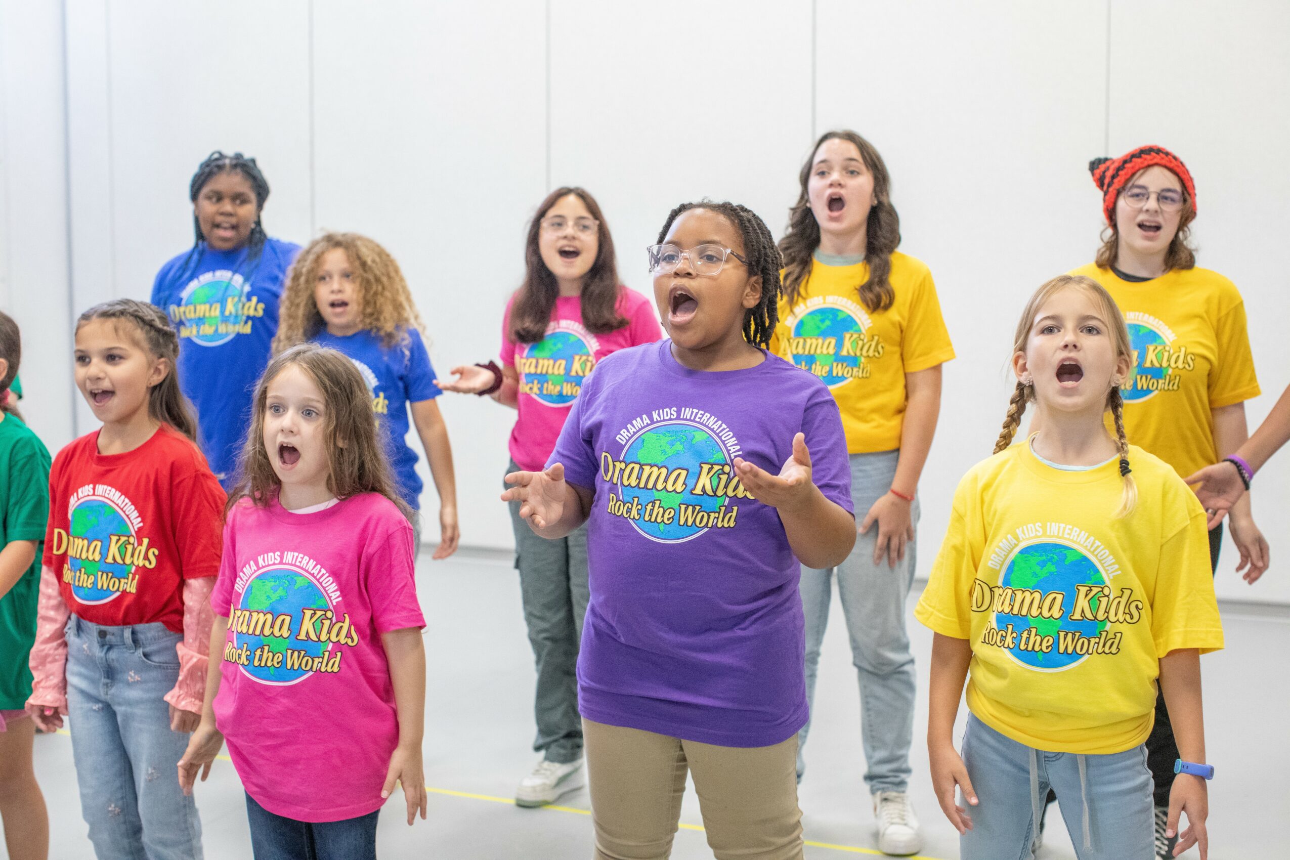 Group of children singing or performing, wearing colorful T-shirts with
