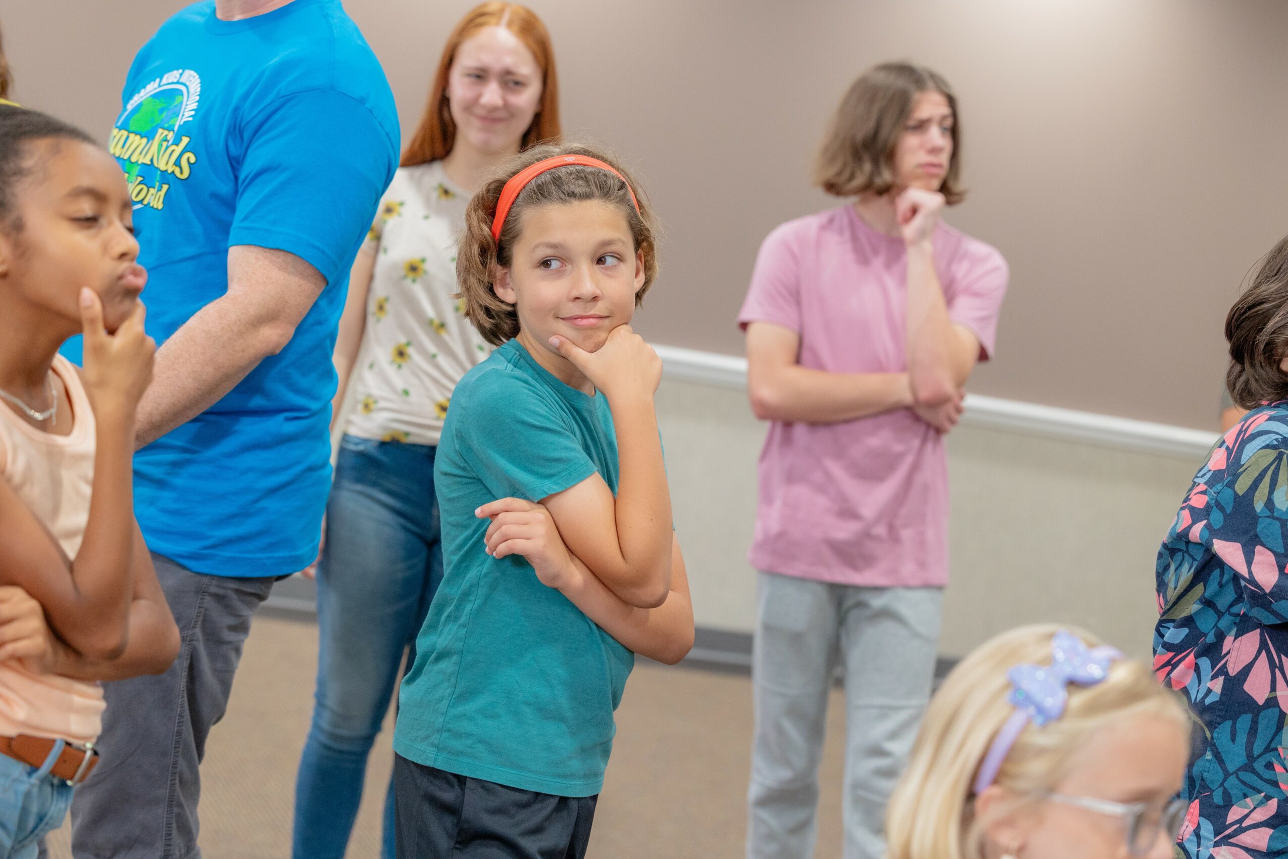 Group of children and adults standing indoors, some children smiling and others looking thoughtful.