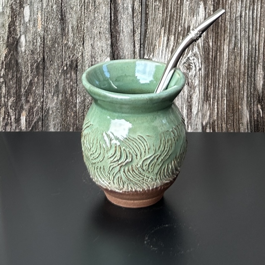 Green ceramic vase with a spoon inside, placed on a black surface against a wooden background.