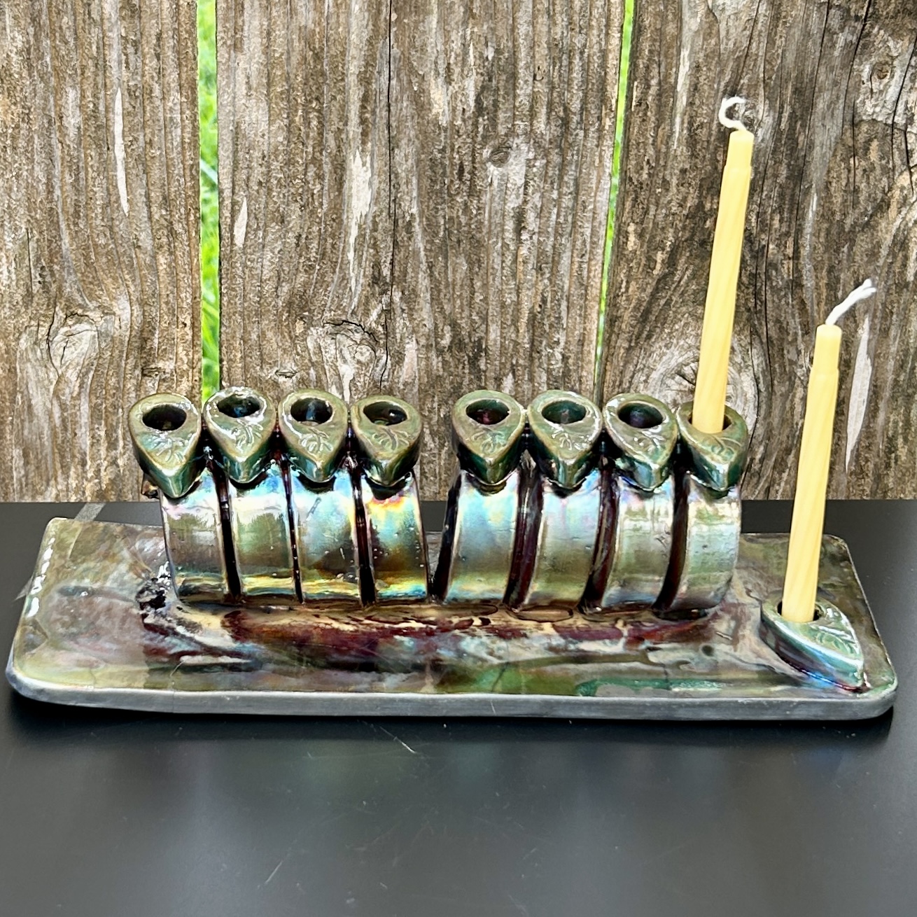 Ceramic candle holder with nine frog-shaped holders and two yellow candles on a rectangular tray, against a wooden background.