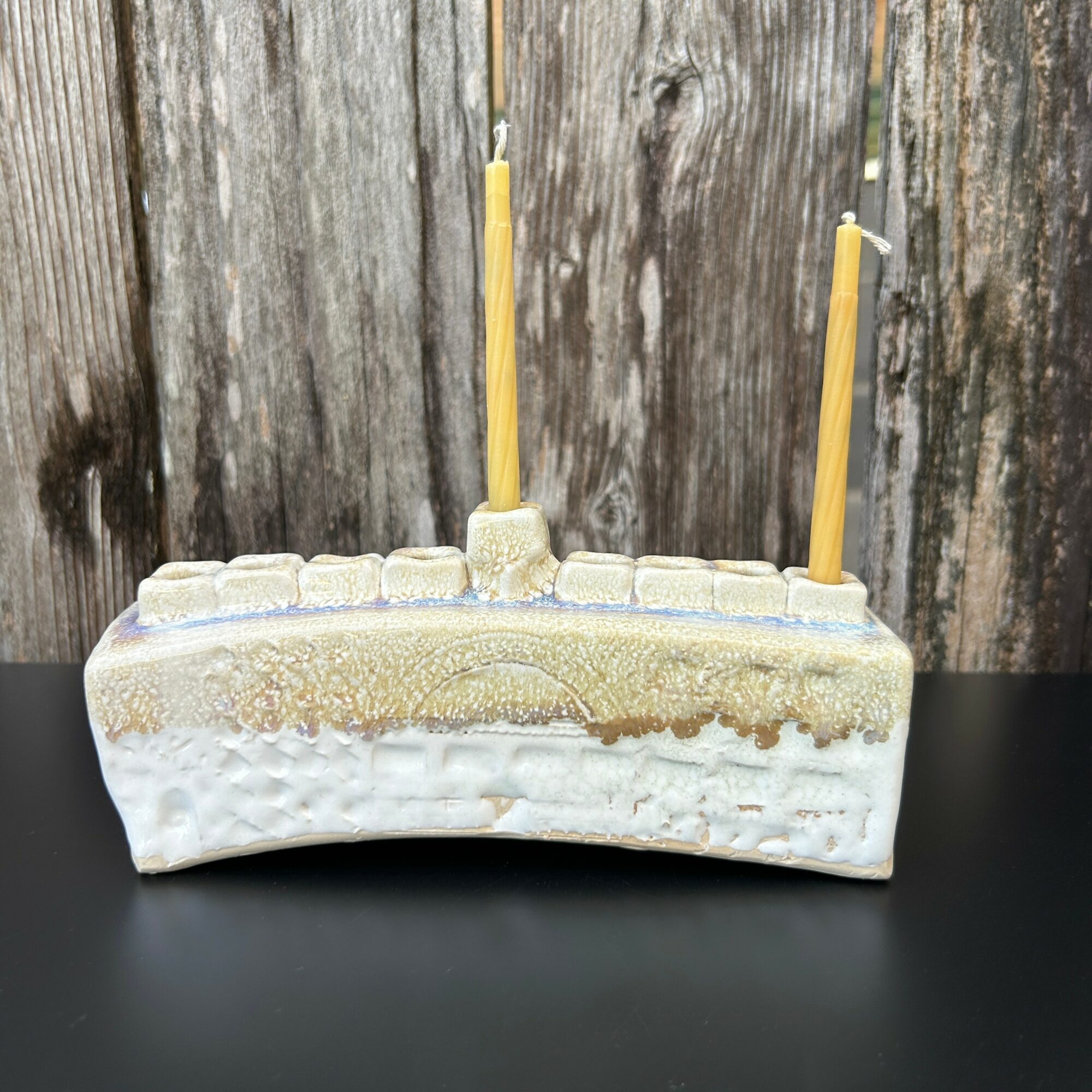 A rectangular cake with two yellow candles on top, placed on a black surface against a wooden background.