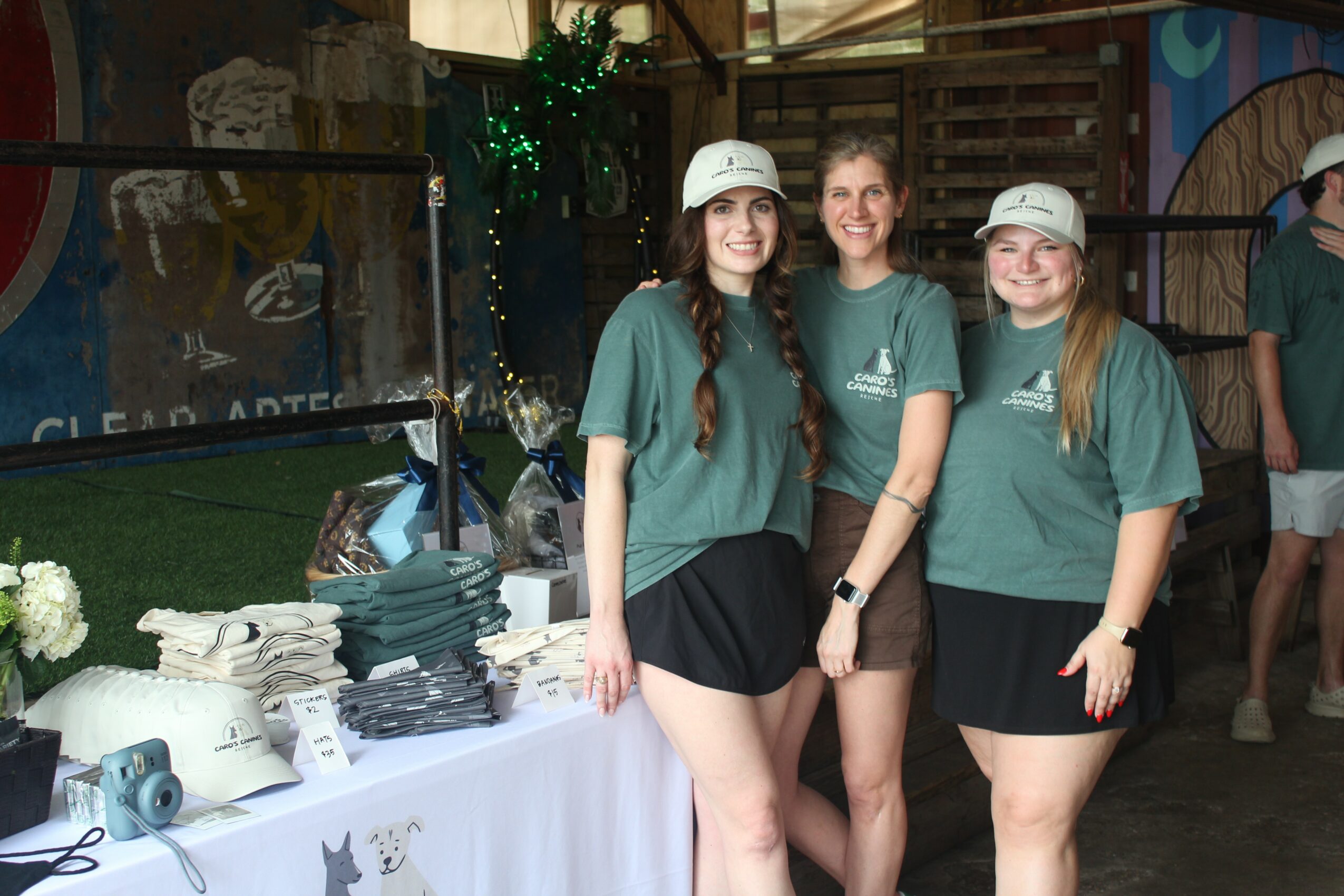 Three women in matching teal shirts and black skirts stand together indoors, smiling for the photo.