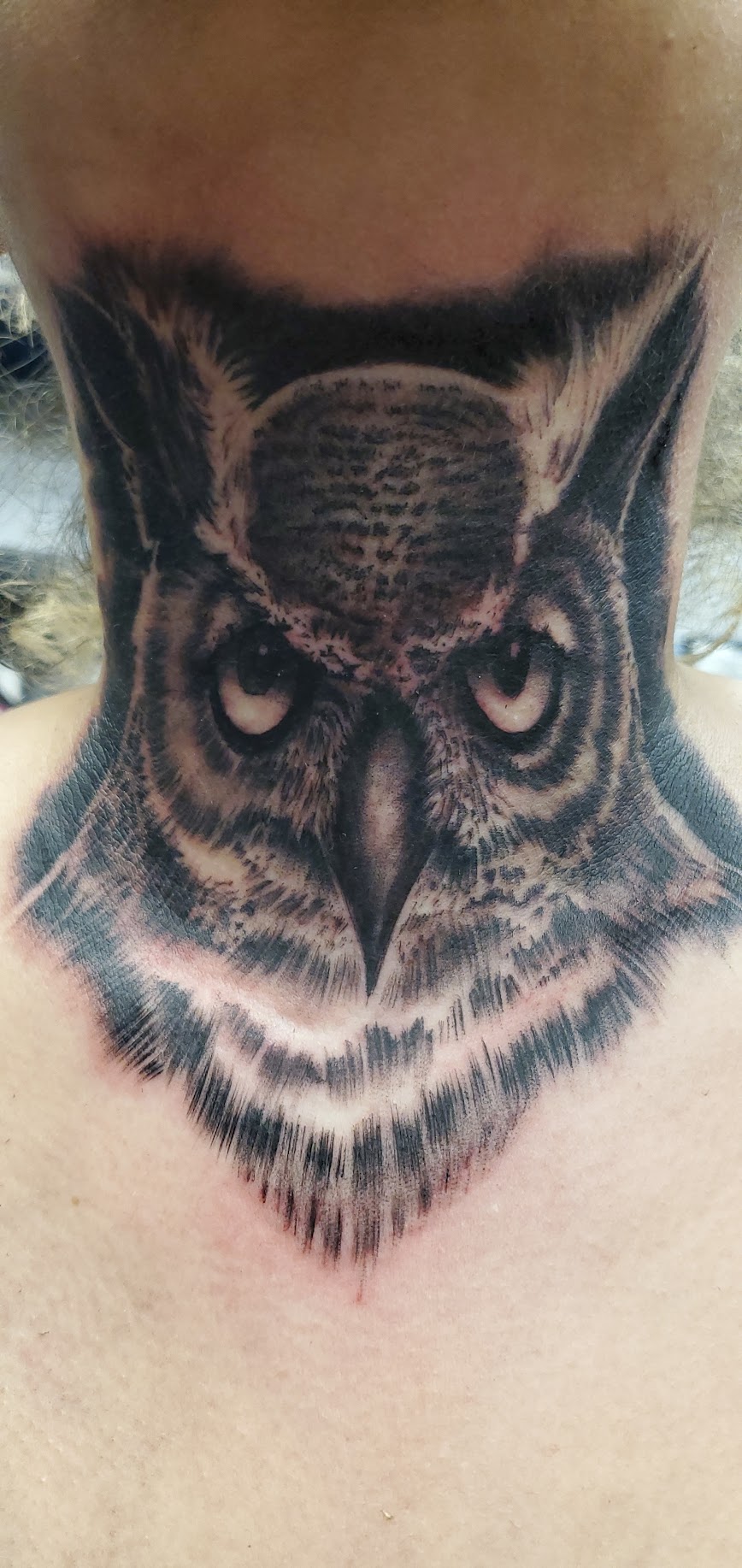 Tattoo of an owl's face with detailed feathers and piercing eyes on person's chest.