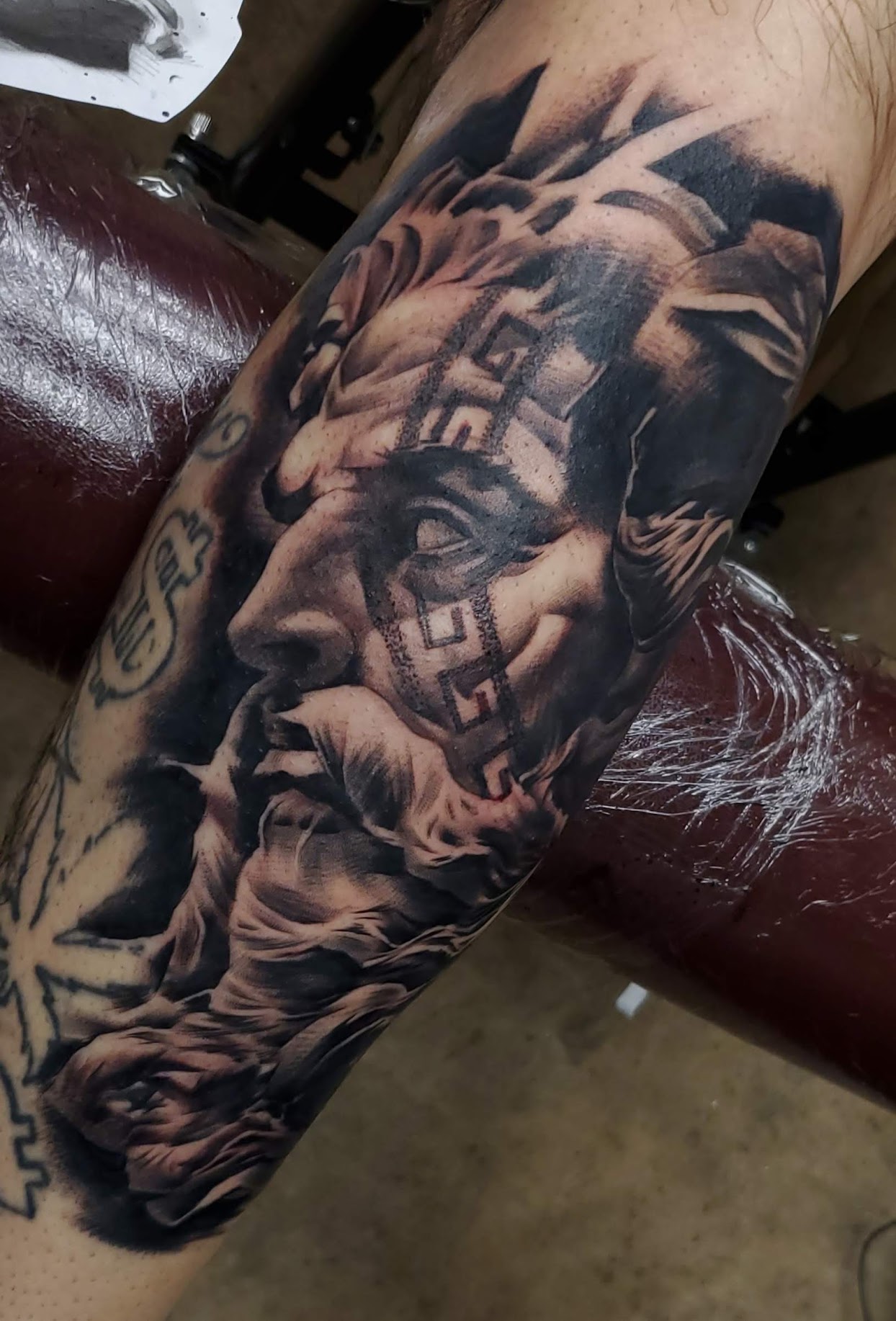 Detailed black and gray tattoo of a classical statue's face and figure on a person's arm.