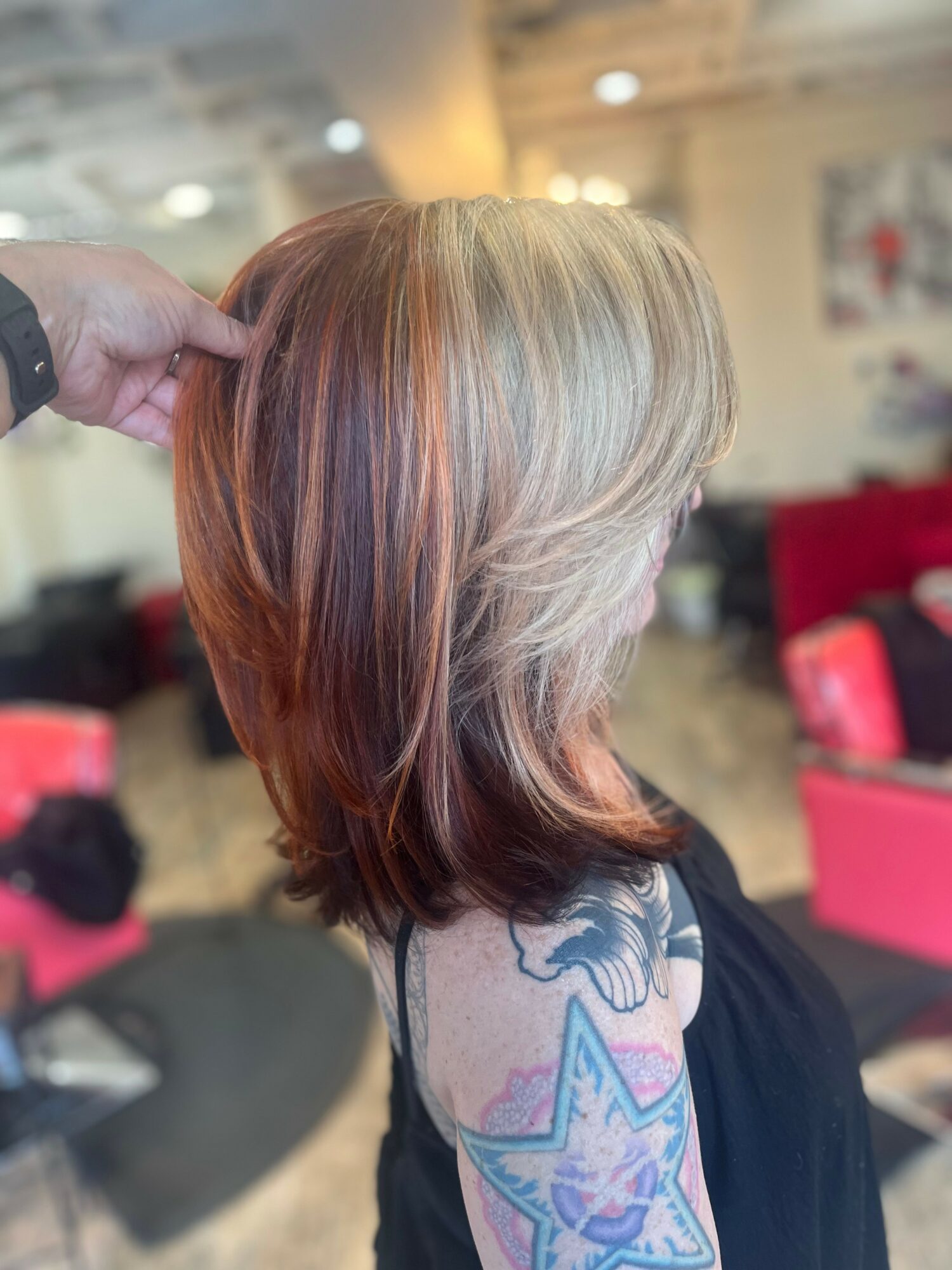 Side view of a woman with shoulder-length blonde and reddish hair, showing a colorful tattoo on her upper arm.