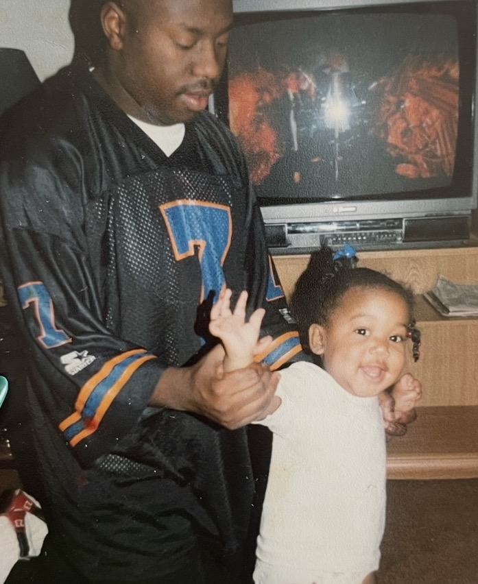 Adult holding a child's hand, both smiling, in front of a television screen showing a fiery scene.