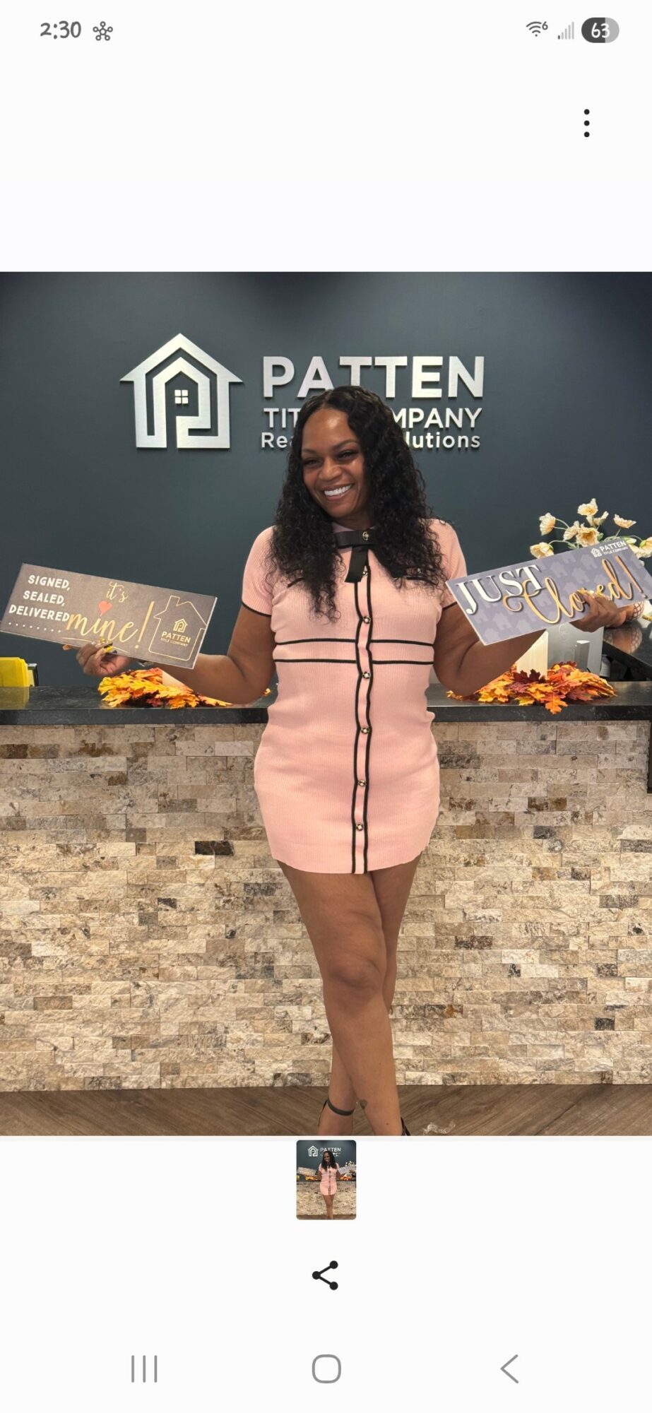Woman in pink dress holding boxes, standing in front of a brick counter with a logo and text, smiling.