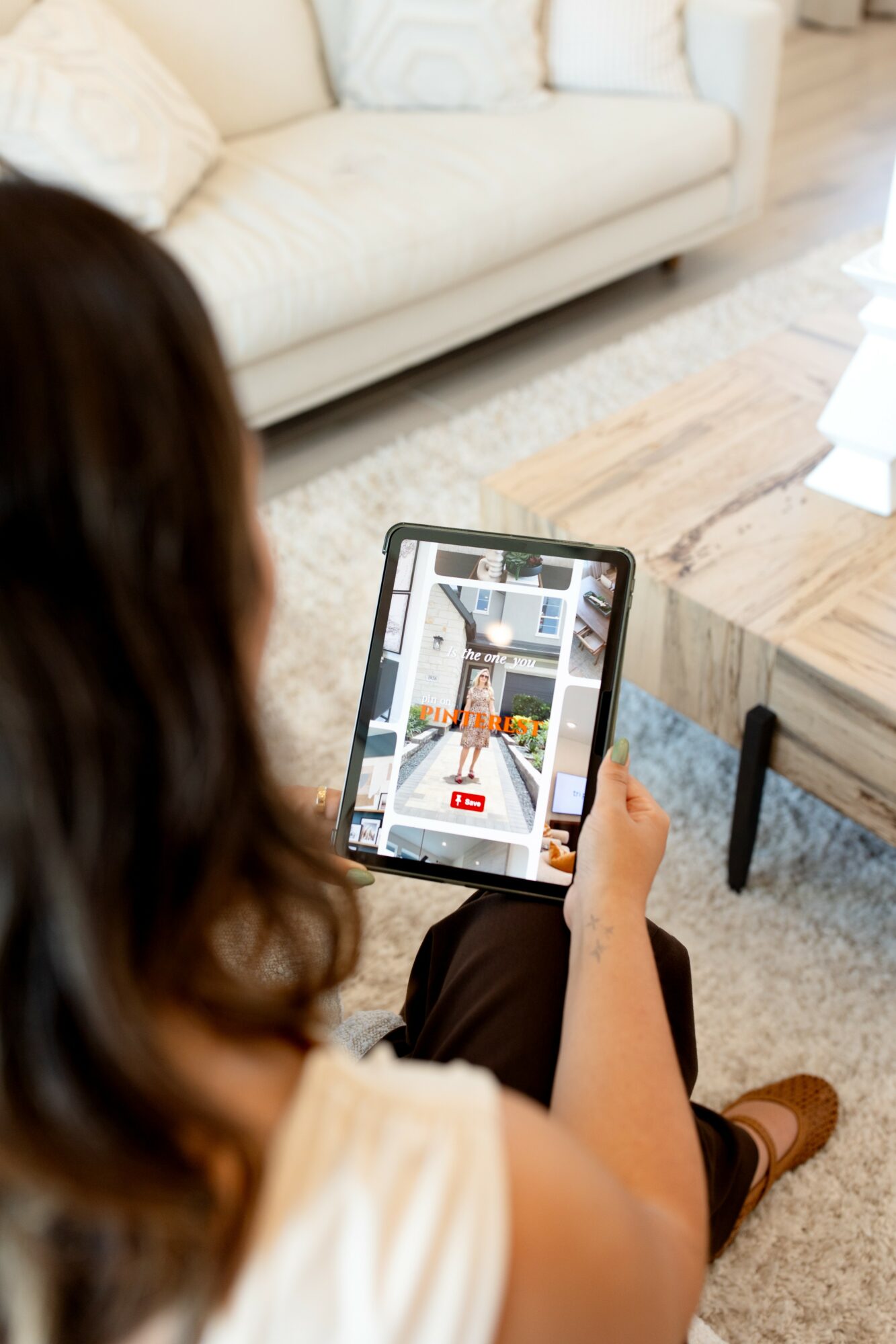 Person holding a tablet showing a room interior with furniture and decor, sitting on a sofa in a living room.