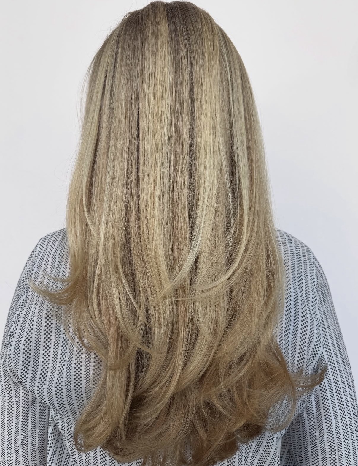 Back view of long, layered blonde hair with subtle highlights, worn by a person in a striped shirt.