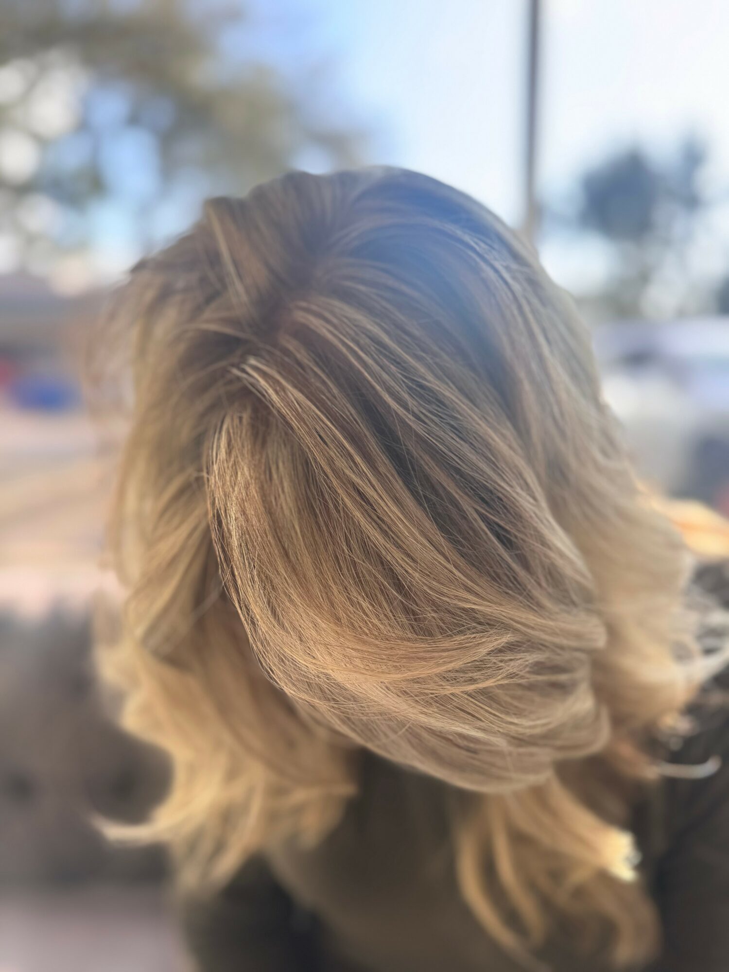 Person with shoulder-length, wavy blonde hair, viewed from above, outdoors with blurred background.