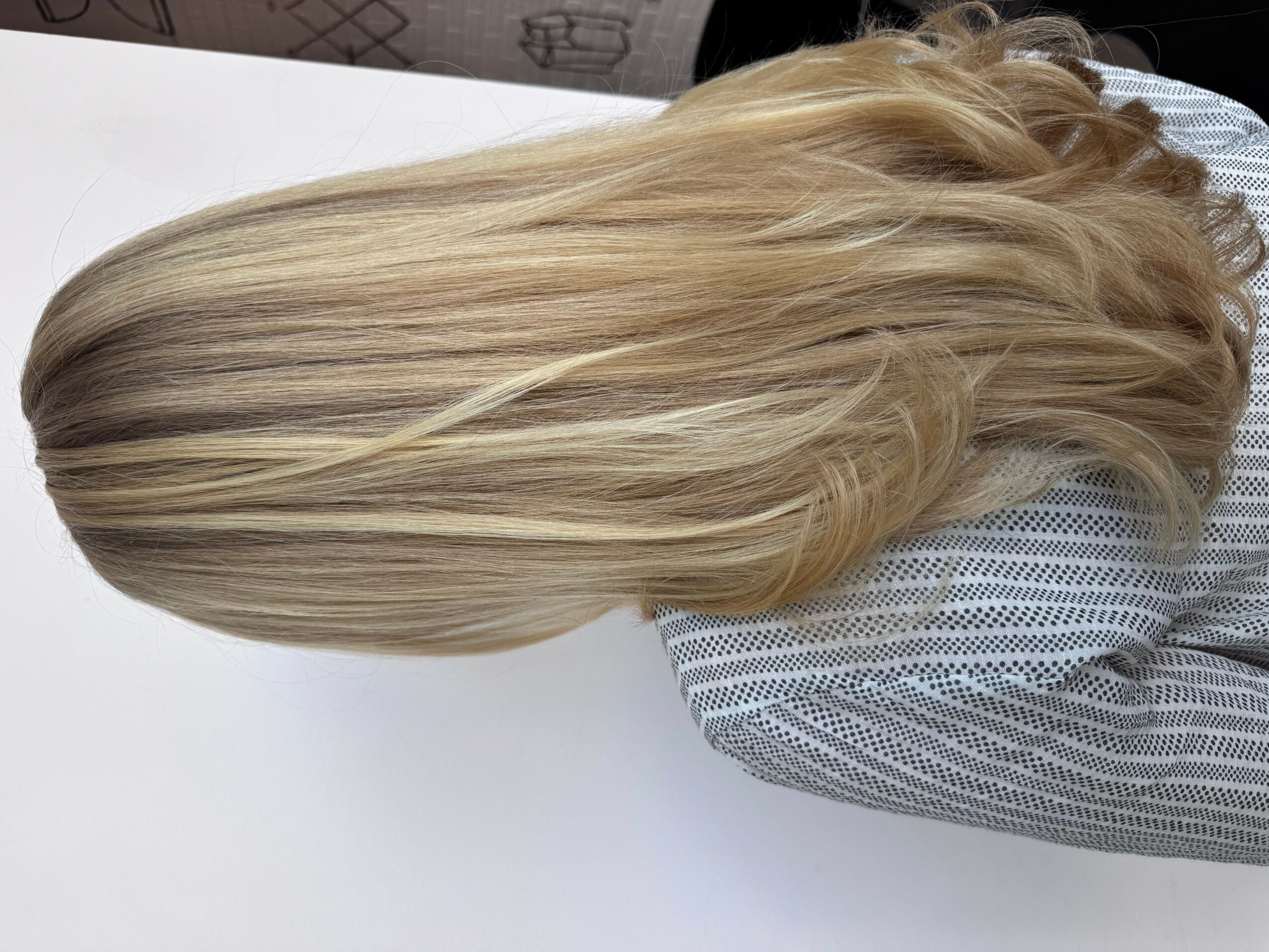 Person with long, blonde, wavy hair wearing a striped shirt, viewed from the side, hair flowing over shoulder.