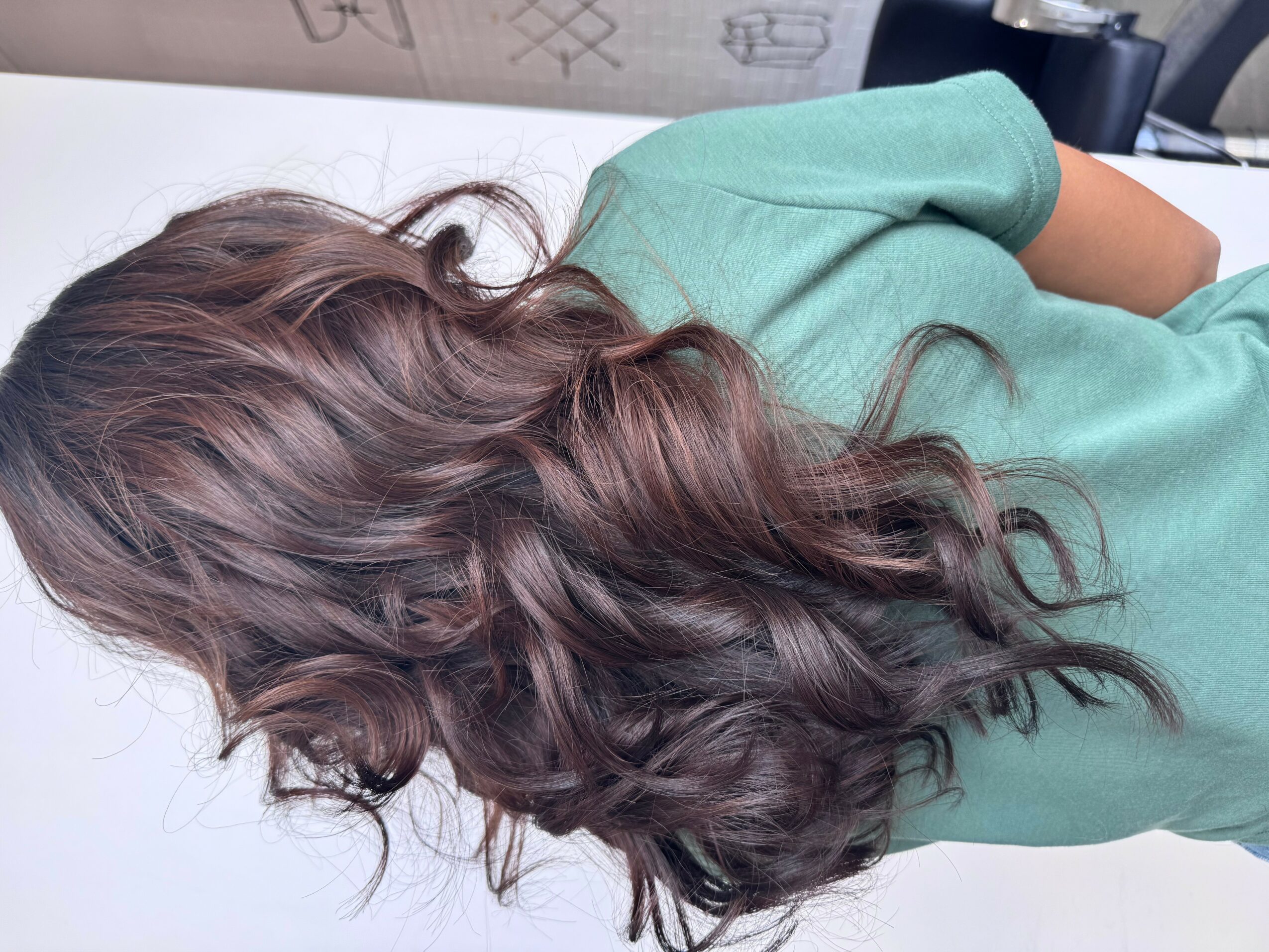 Person with long, wavy brown hair wearing a green shirt, facing away from the camera.