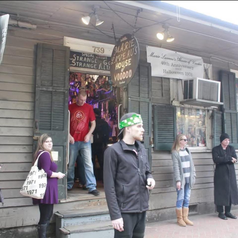 People standing outside a building with a sign for a haunted house attraction, some wearing jackets and boots, one person with a green hat.