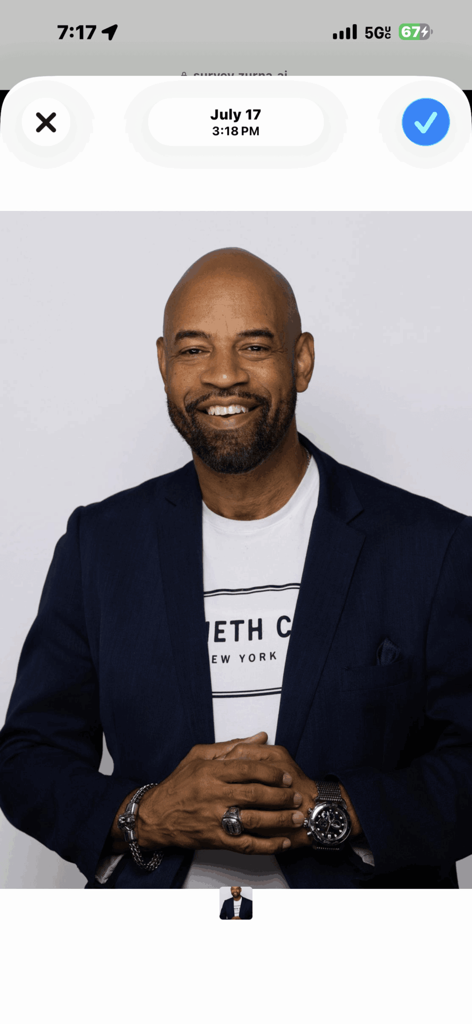 Man with a beard and bald head smiling, wearing a dark blazer and white shirt, against a plain background.
