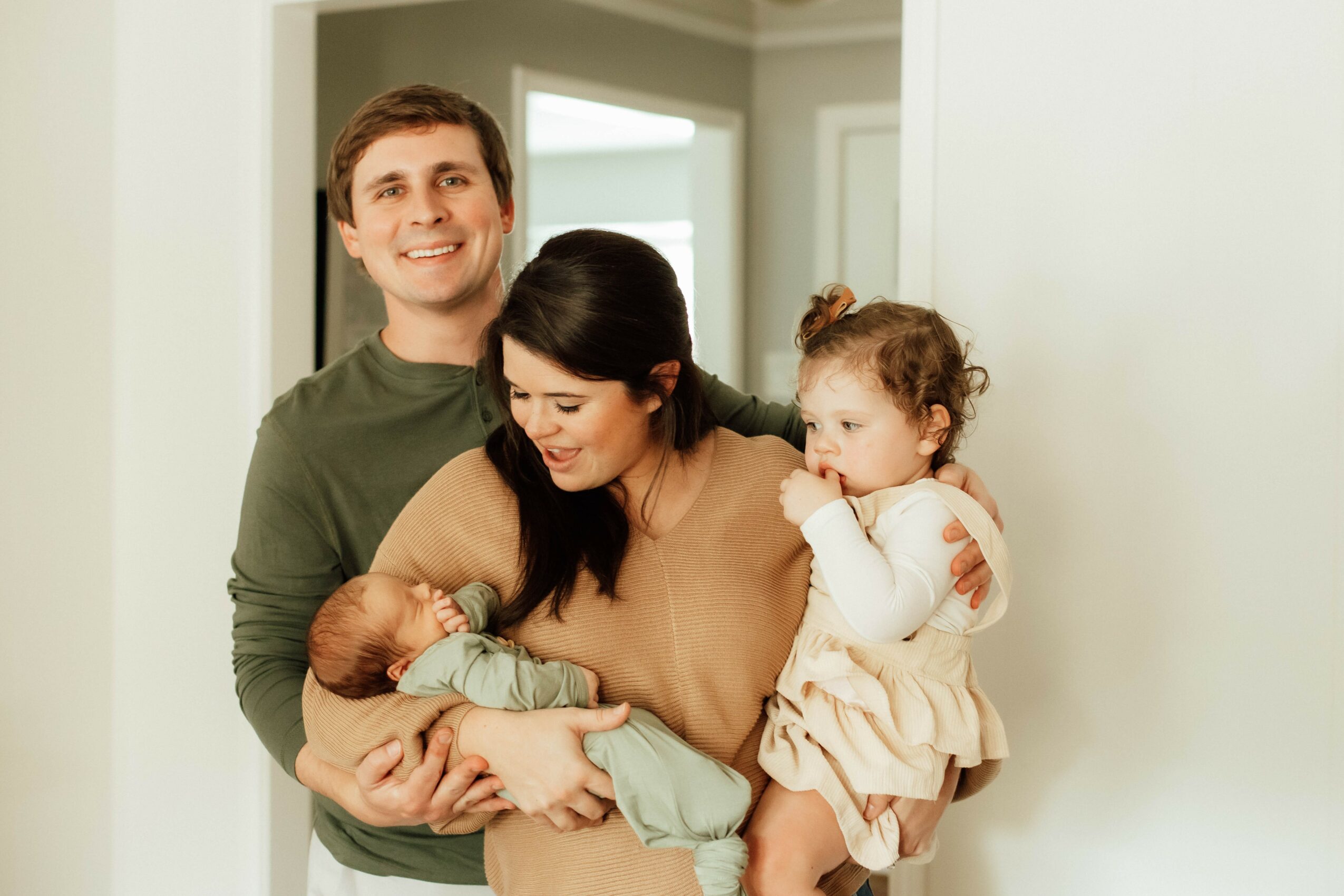 Family of four with two children, one baby and one toddler, inside a home, smiling and interacting.