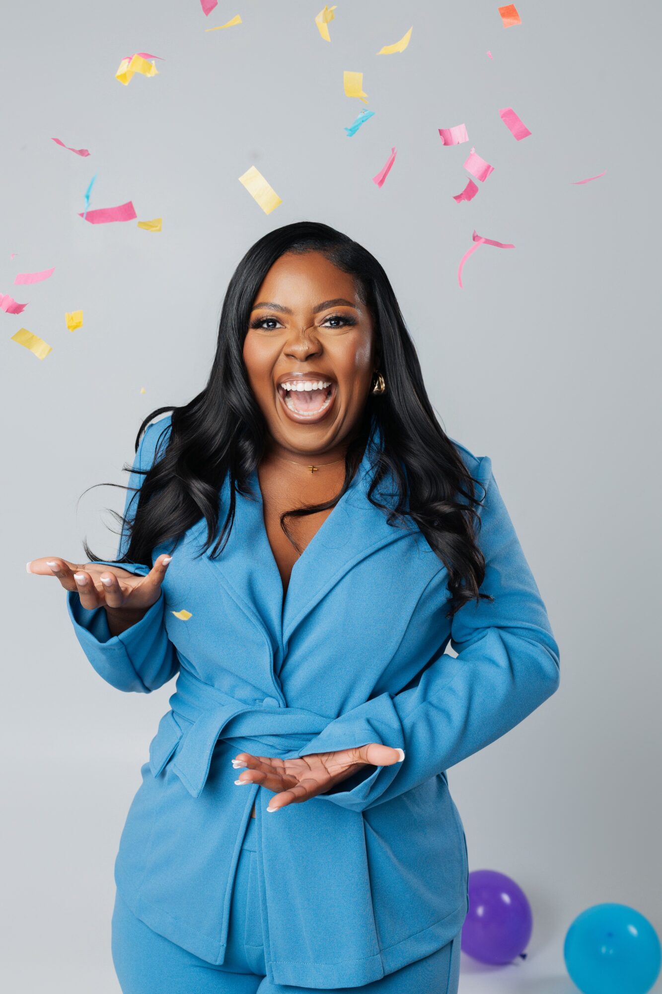 Woman in blue coat smiling with confetti falling around her, gray background.