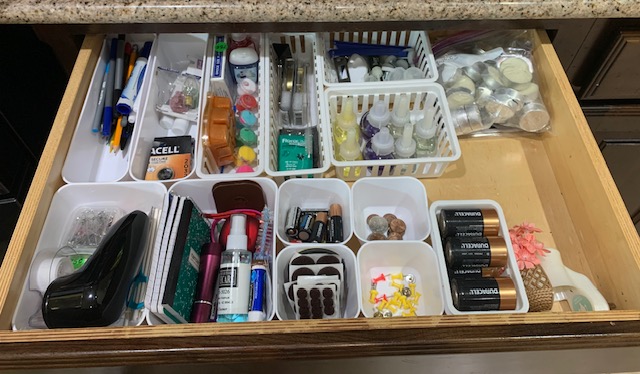Open drawer with organized nail polish, tools, and supplies in white containers on a wooden surface.