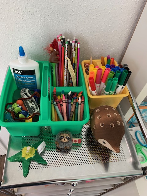 Desk with colorful markers, notebooks, a plush toy, a decorative cactus, and a brown stuffed animal on a metal surface.