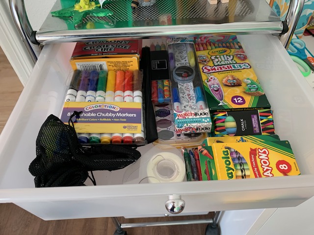 Open drawer with colorful school supplies, including markers, glue, and craft items, organized inside.