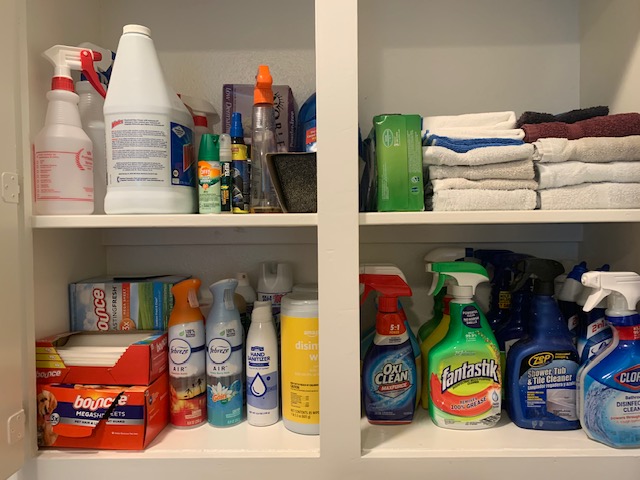 Open cabinet with cleaning supplies, towels, and containers on shelves.