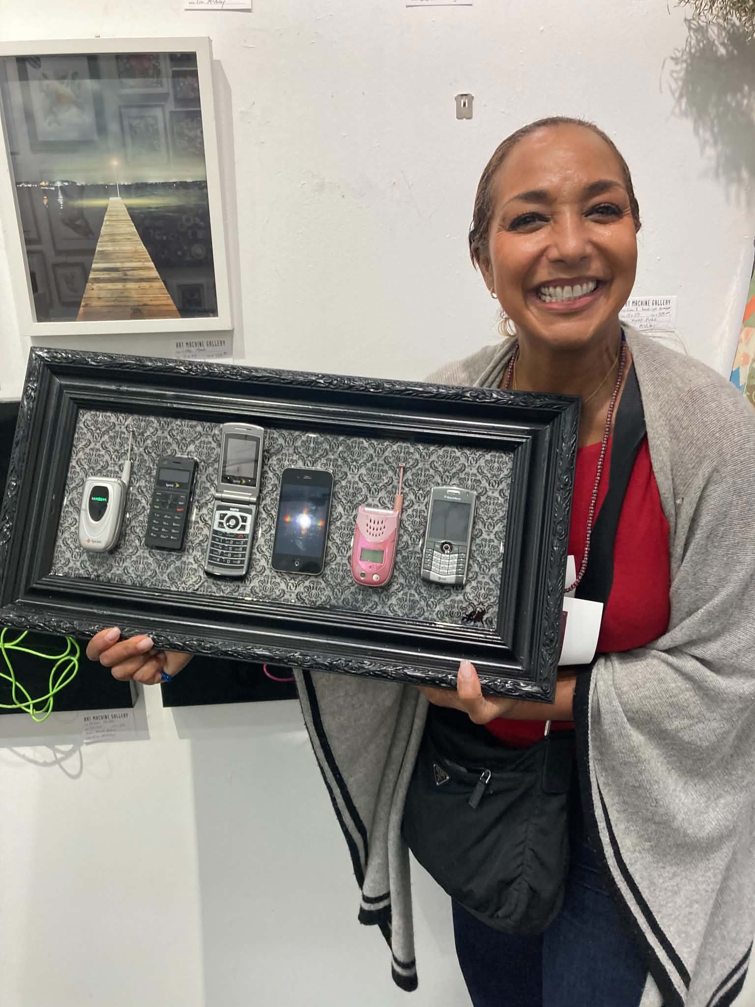 Smiling woman holding a display case with five different mobile phones, standing indoors.