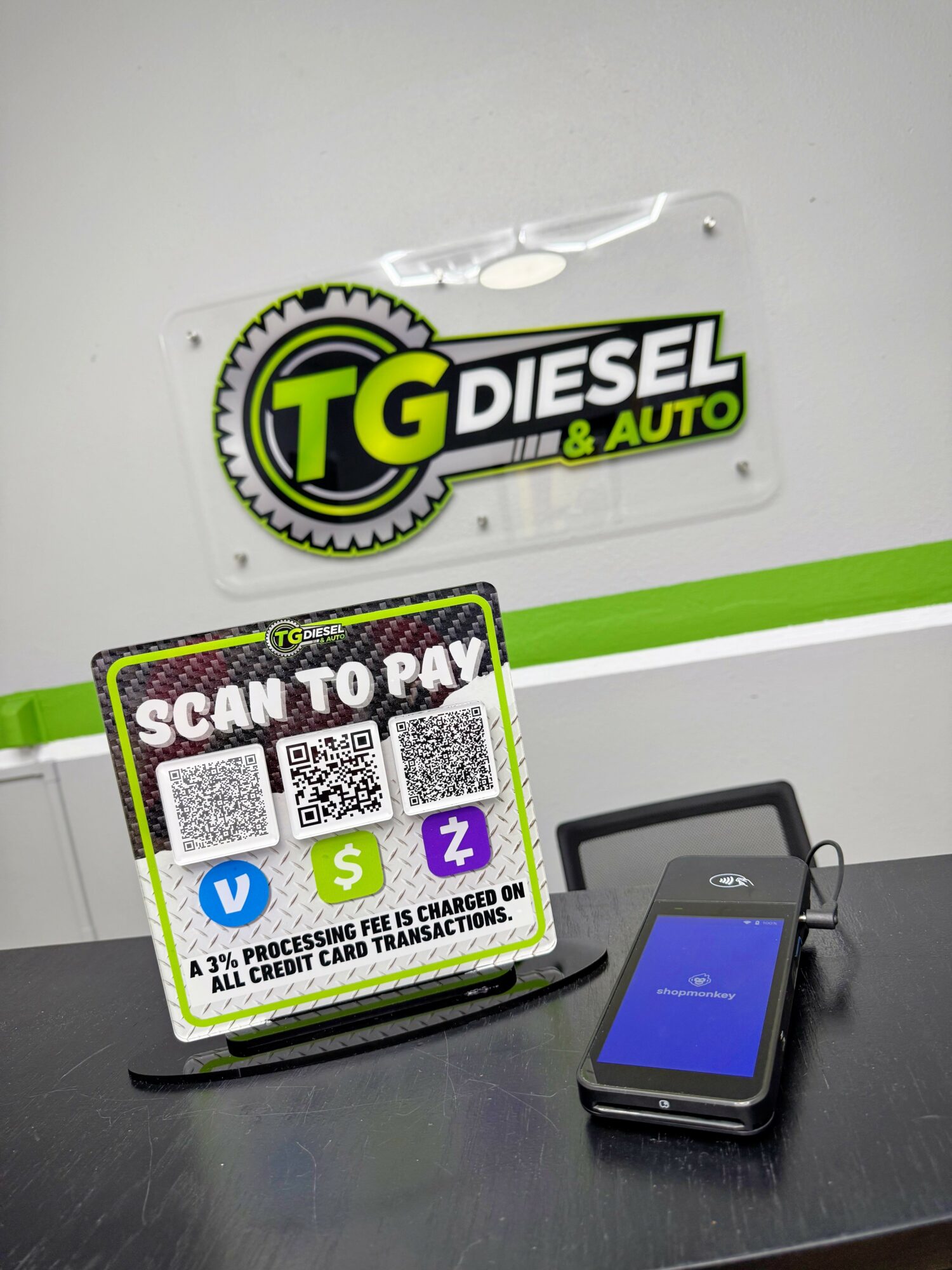 TG Diesel & Auto sign, QR code payment sign, smartphone on table, plain background.