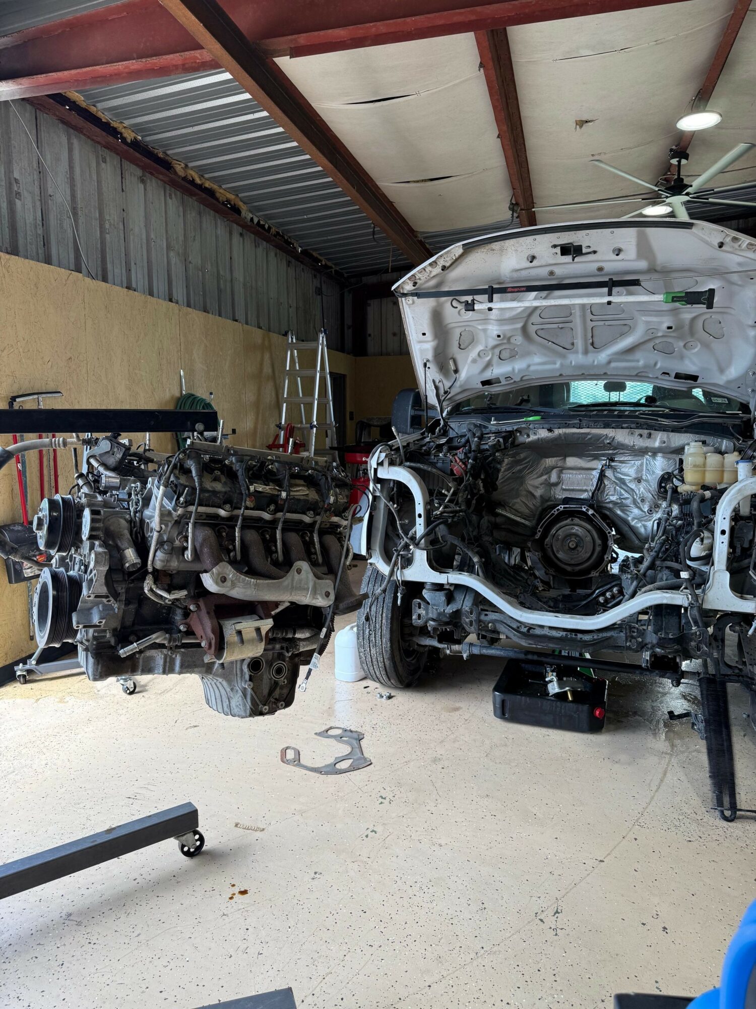 Two disassembled car engines on a workshop floor with tools and parts around them.
