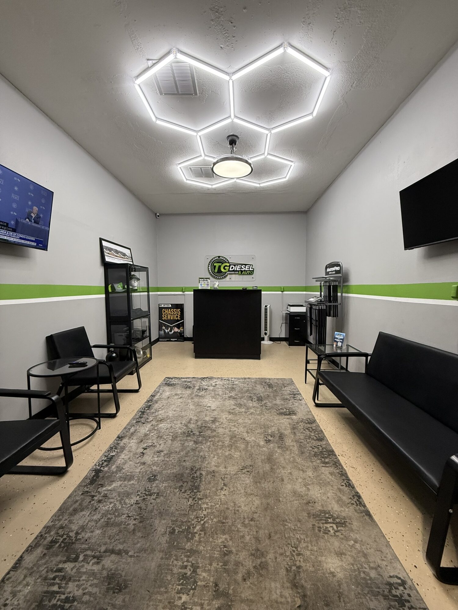 Office room with modern hexagon-shaped ceiling lights, black chairs, a black sofa, a rug, and a green stripe on the wall.