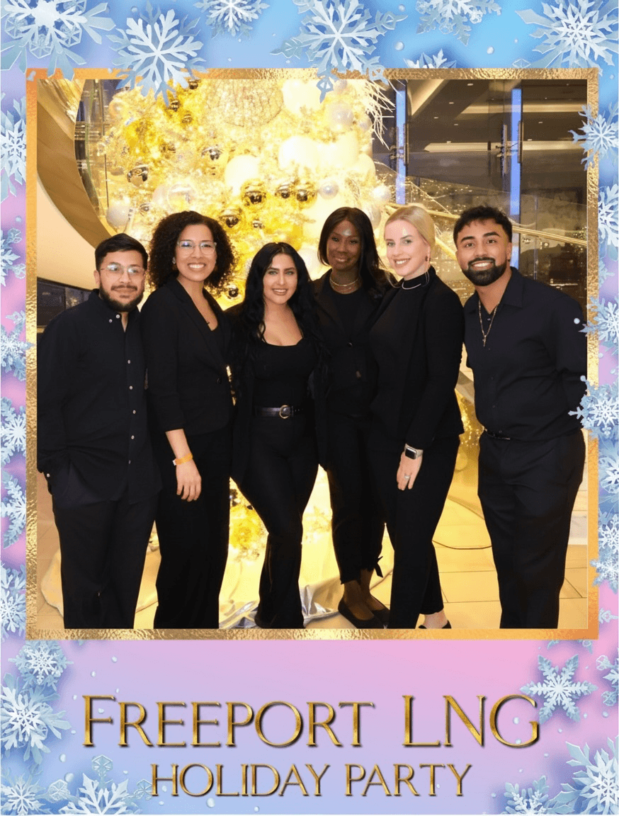 Group of six people dressed in black, standing indoors with a festive background, smiling for a photo, holiday party setting.