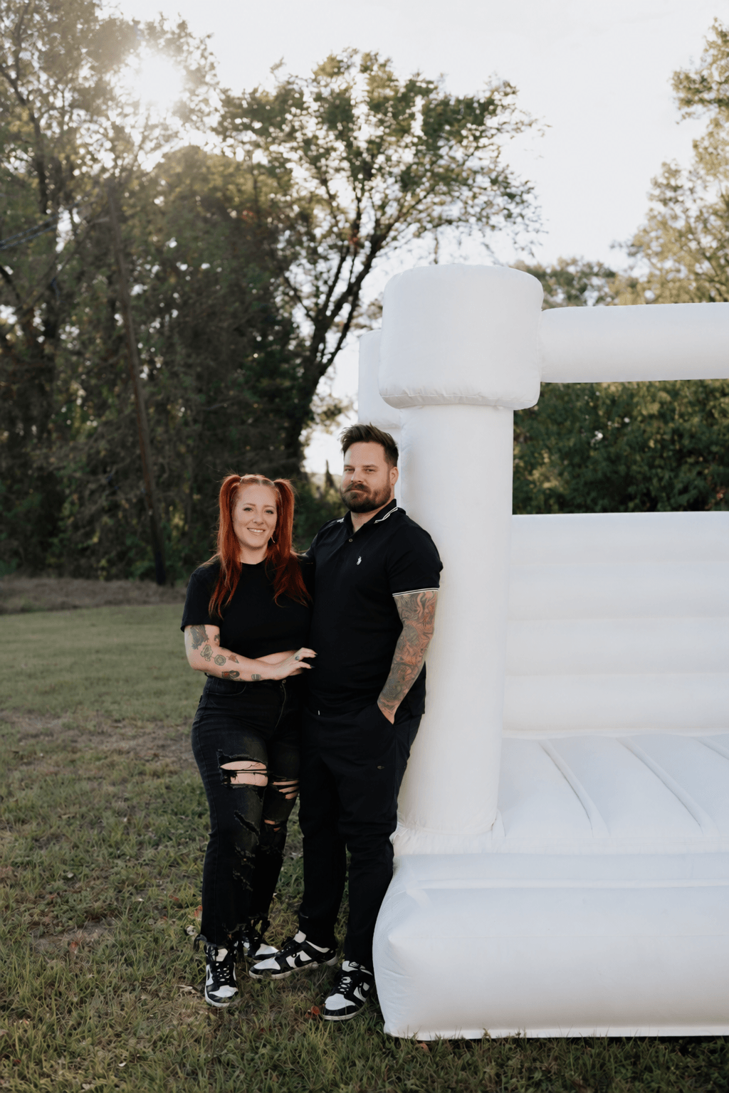 Two people standing outdoors near a large white inflatable structure, with trees and sky in the background.