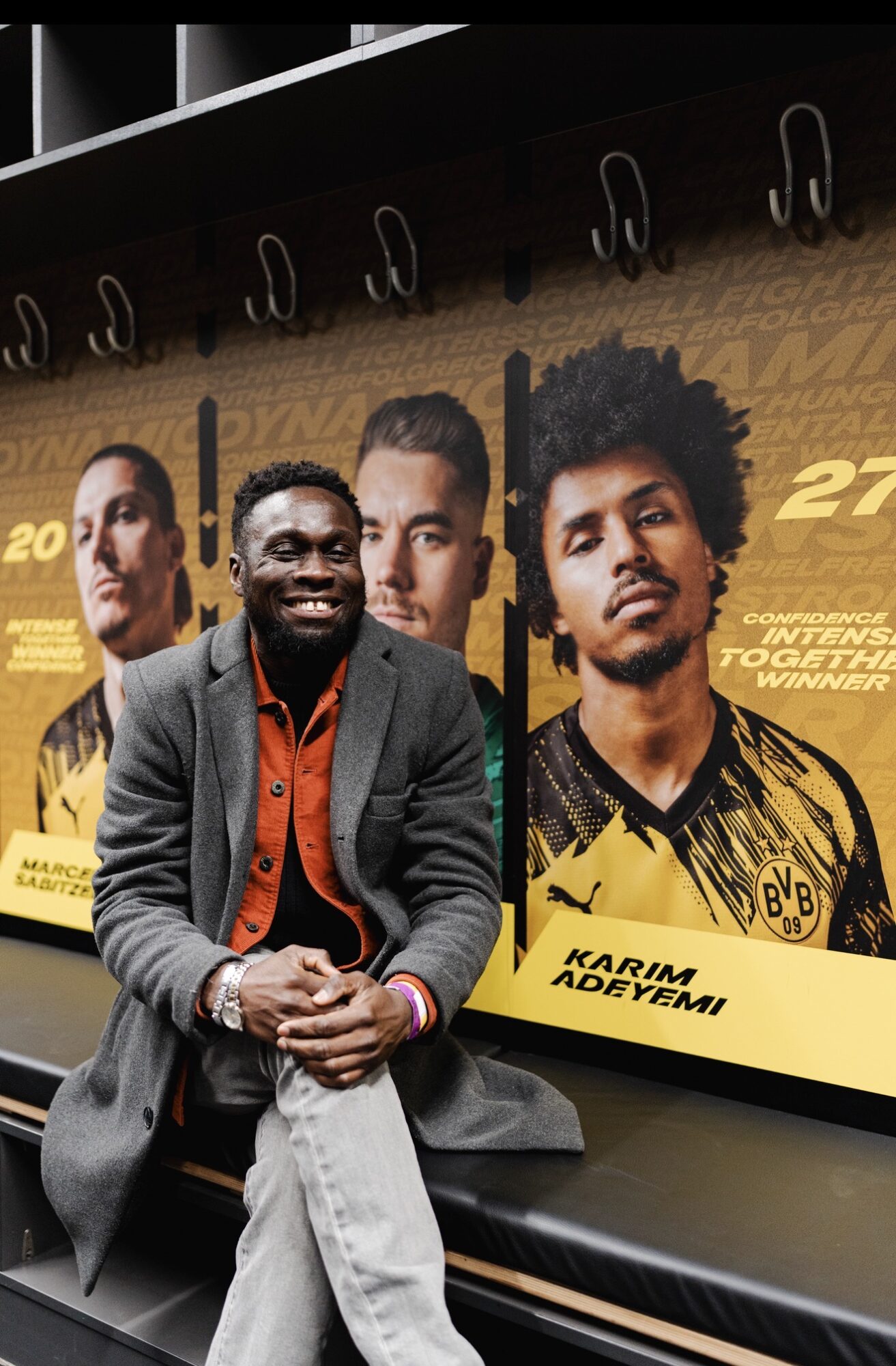 Person sitting on a bench in front of a large poster featuring four football players and text about a match.