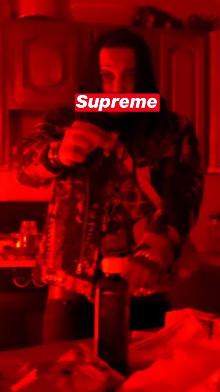 Person taking a selfie in a room with red lighting, holding a bottle, with a