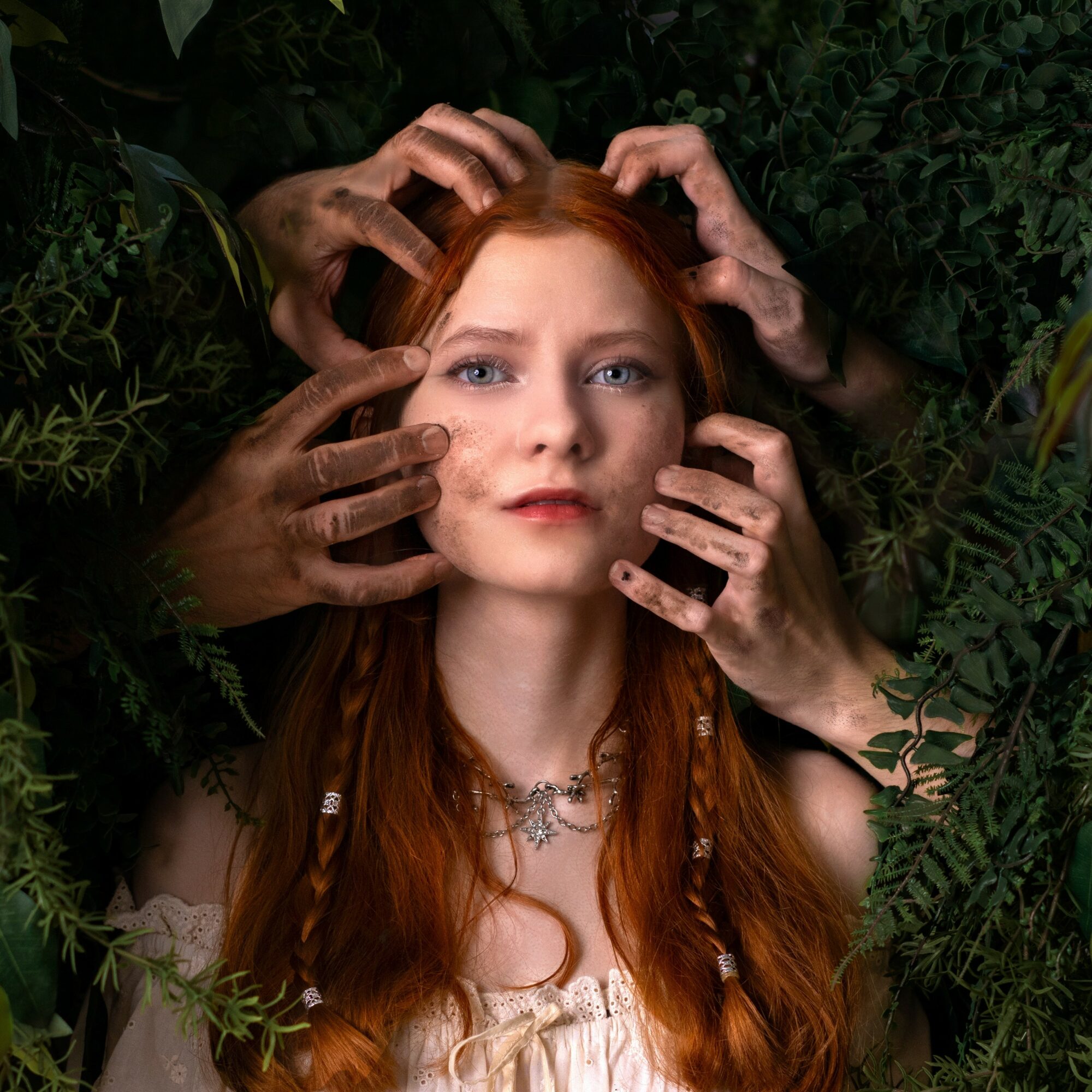 Young woman with long red hair surrounded by multiple hands touching her face and head, greenery in background.
