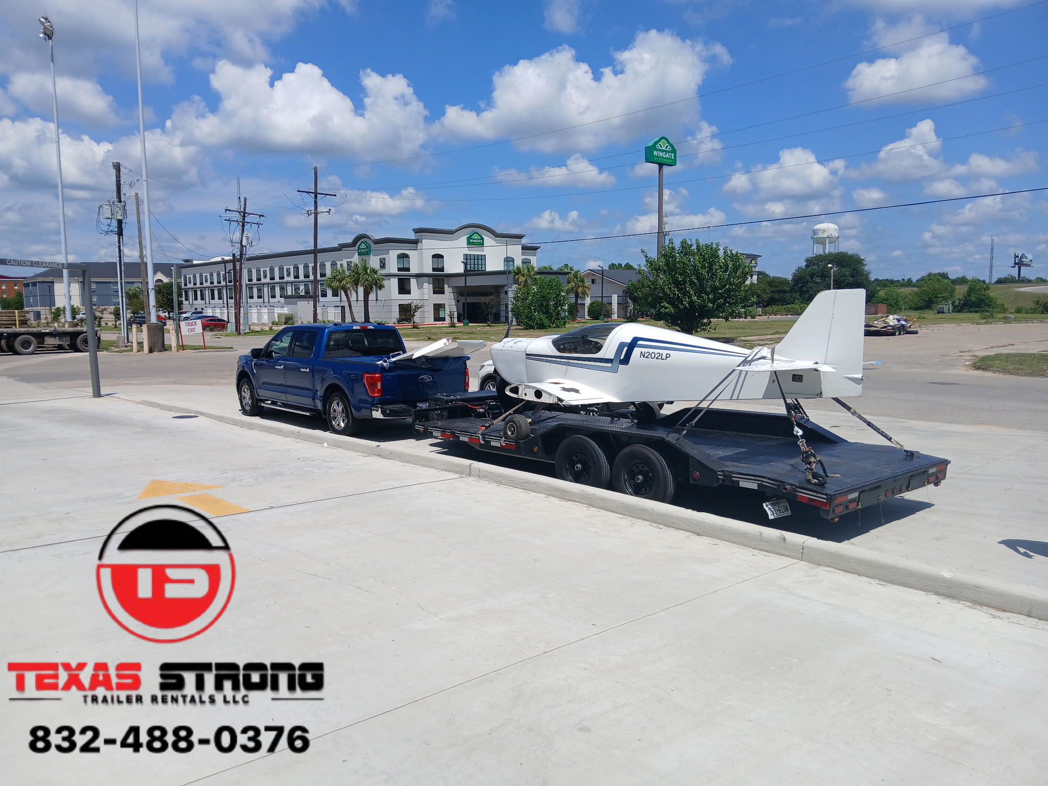 Black pickup truck towing a boat on a trailer parked on a concrete lot with buildings and blue sky in background.