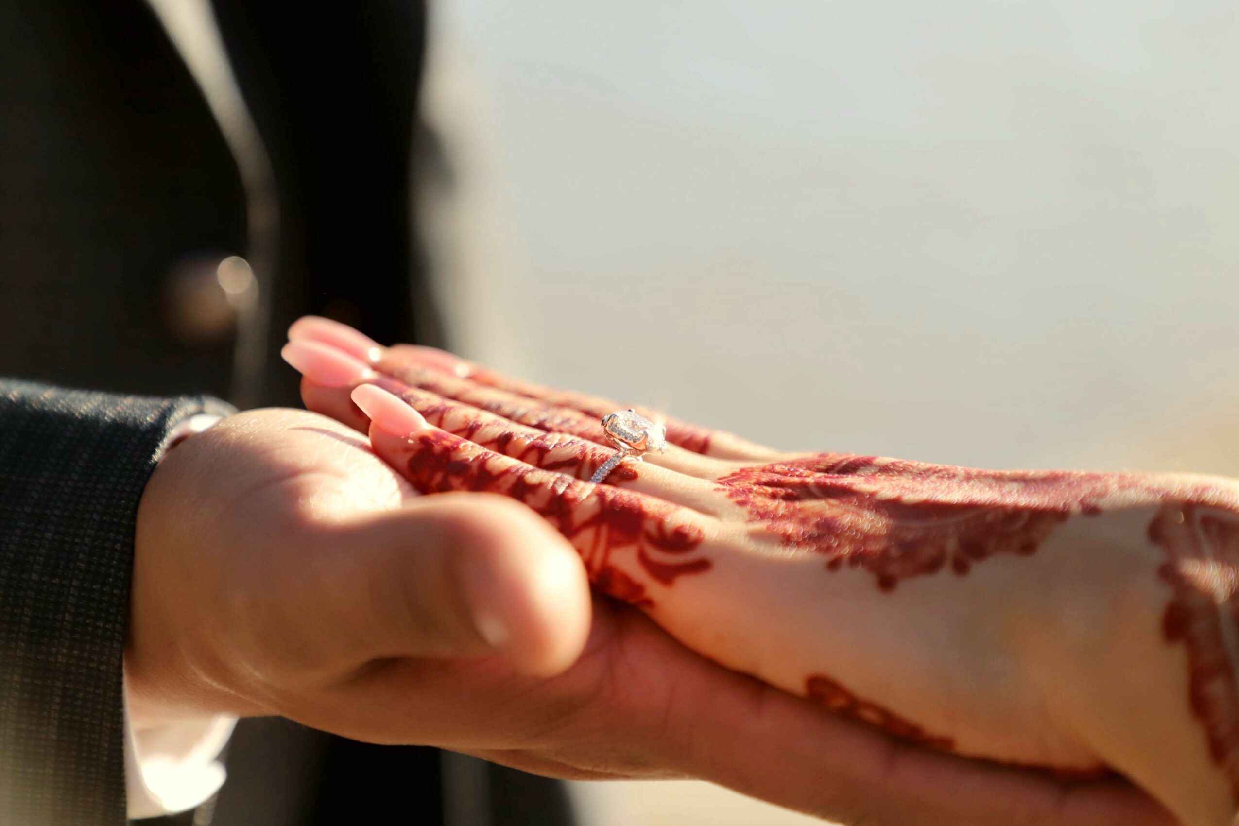 Two hands, one with a ring, hold a large piece of raw meat with visible marbling, outdoors with a blurred background.