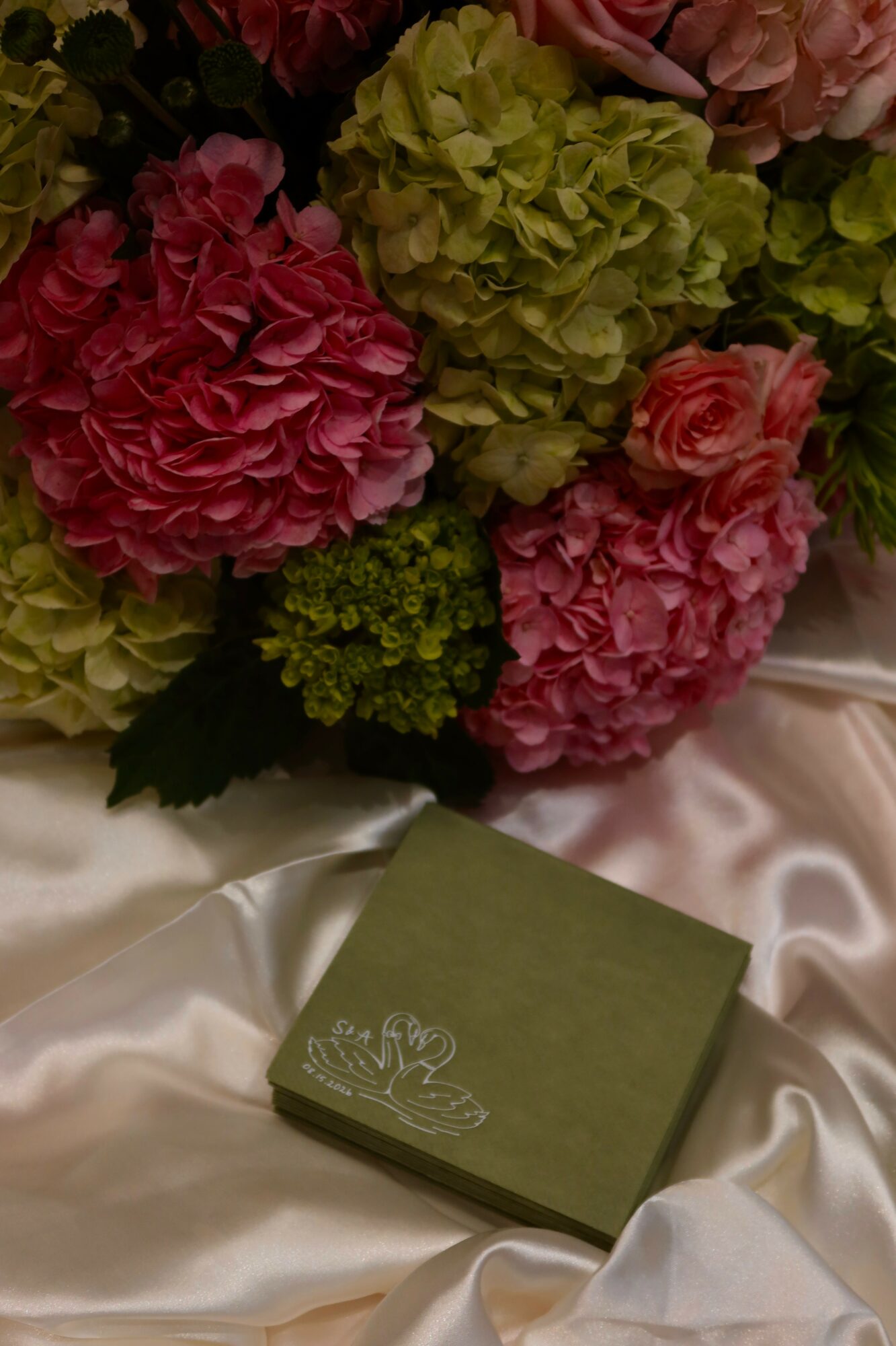 Bouquet of pink and green hydrangeas on satin fabric with a green box nearby.