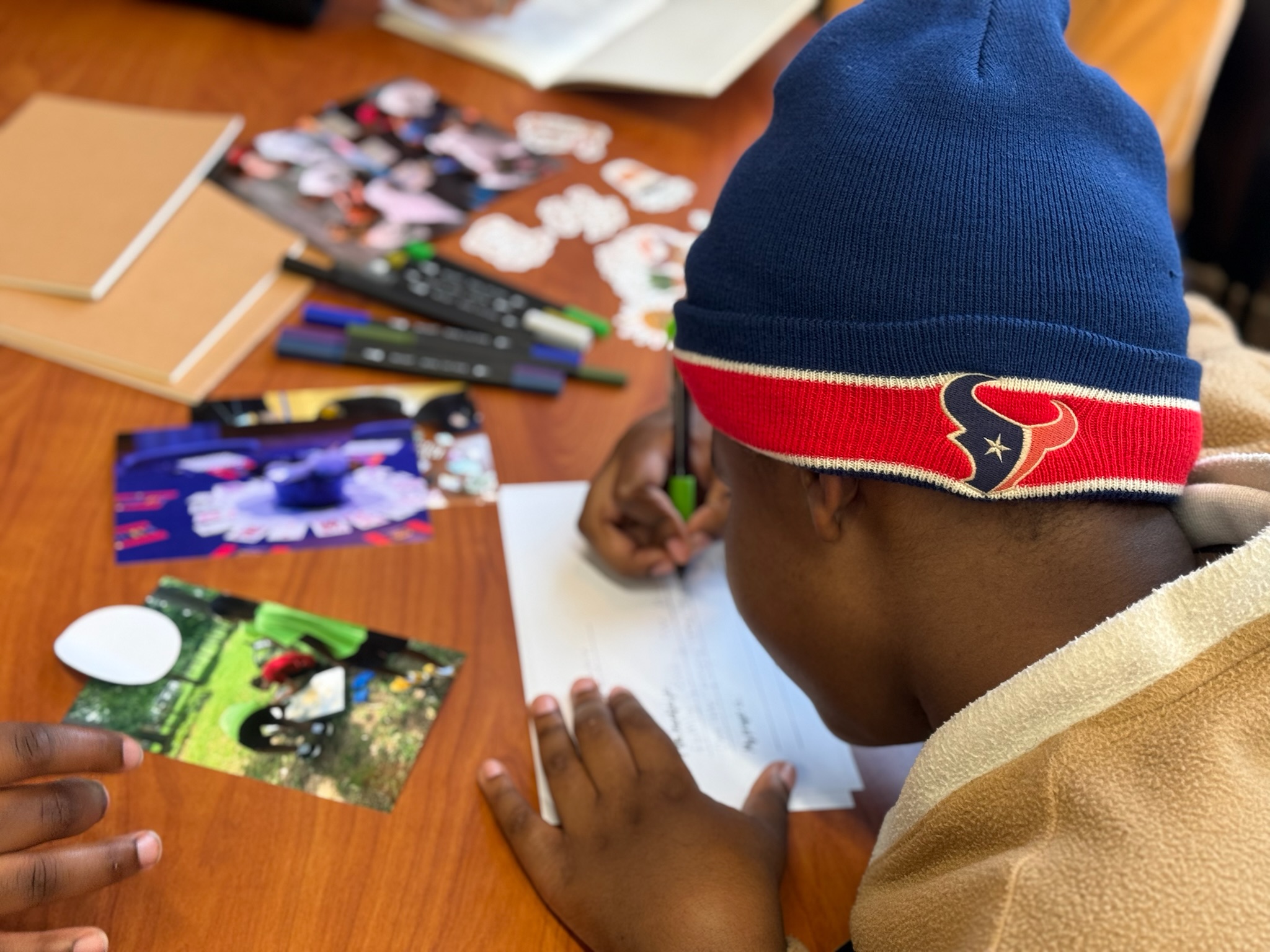Child wearing a blue beanie with a red and white band, working on a craft project at a table.