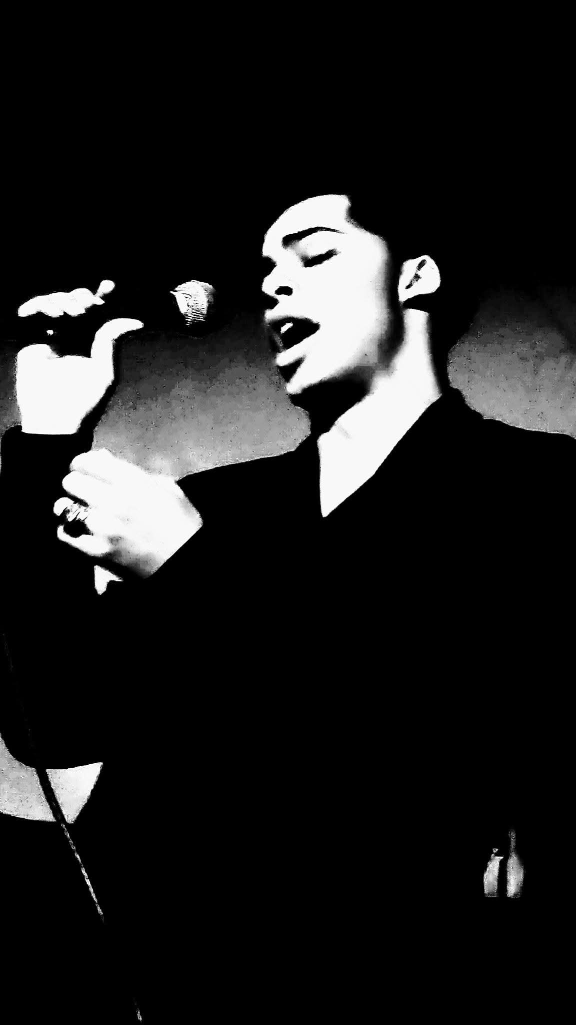 Person singing into a microphone with eyes closed, holding the microphone with one hand, in black and white.